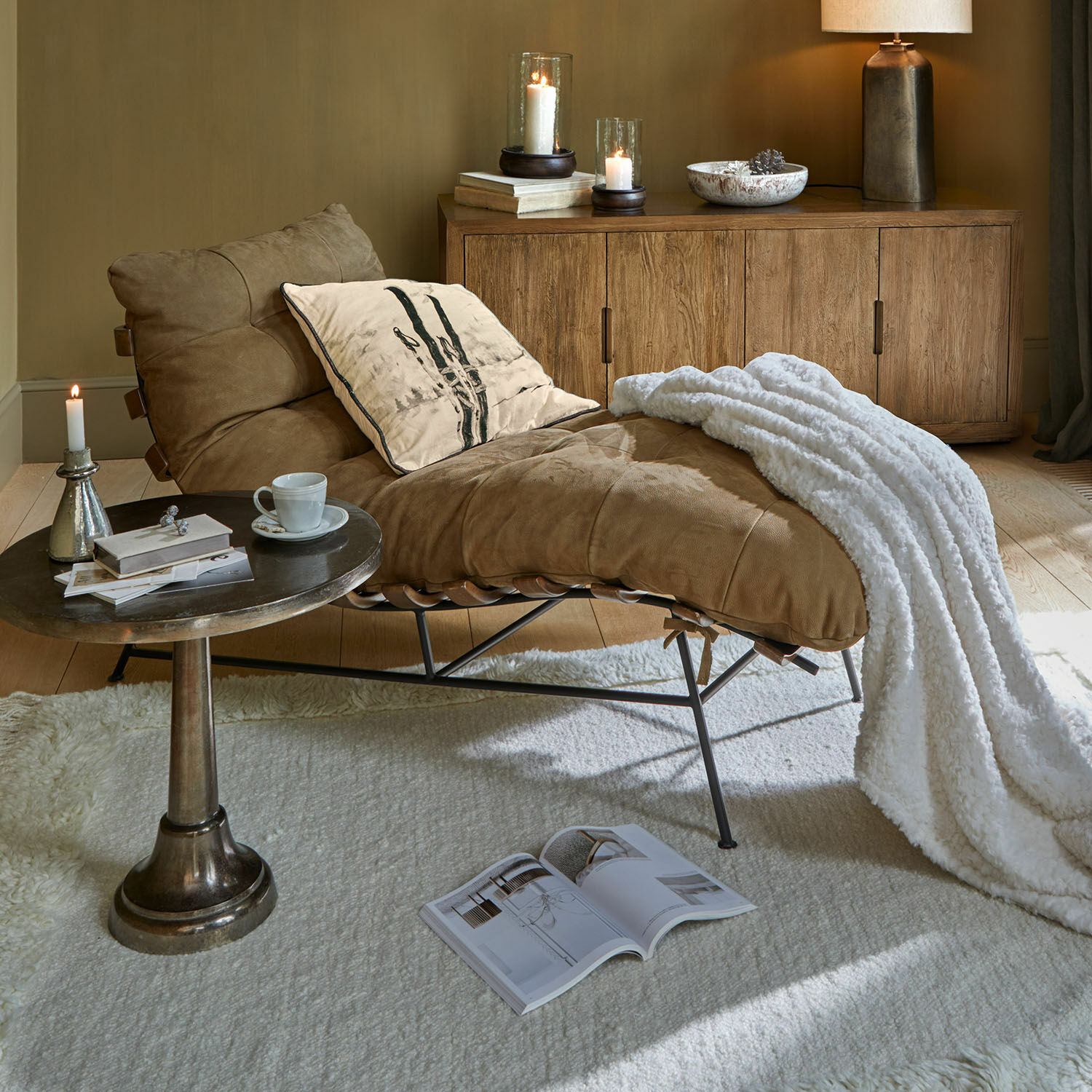Chaise longue Horraine Poltrona in pelle marrone con coperta bianca e cuscino vicino a mobile in legno e tavolino