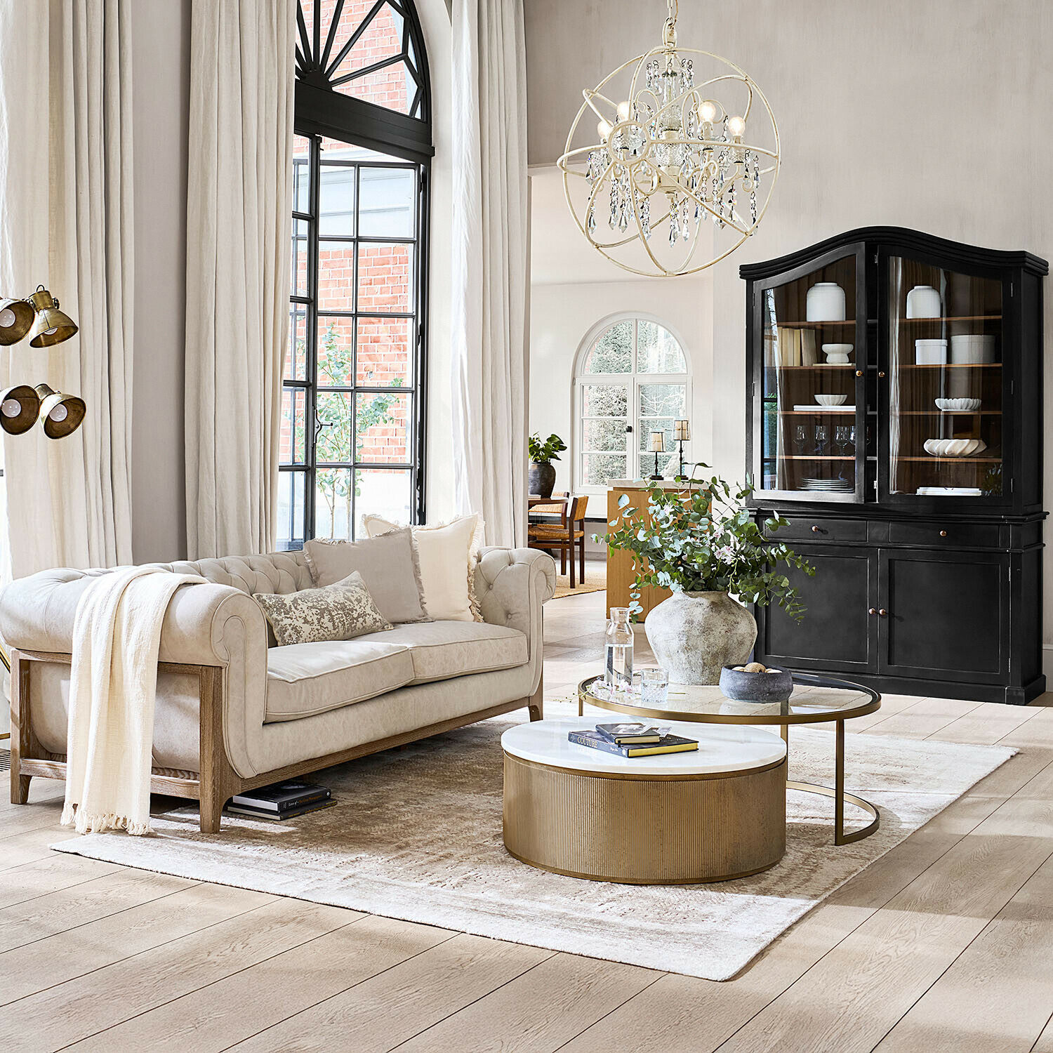 Tappeto Ashmere Divano beige confortevole con struttura in legno in soggiorno luminoso con vetrina nera e tavolino dorato