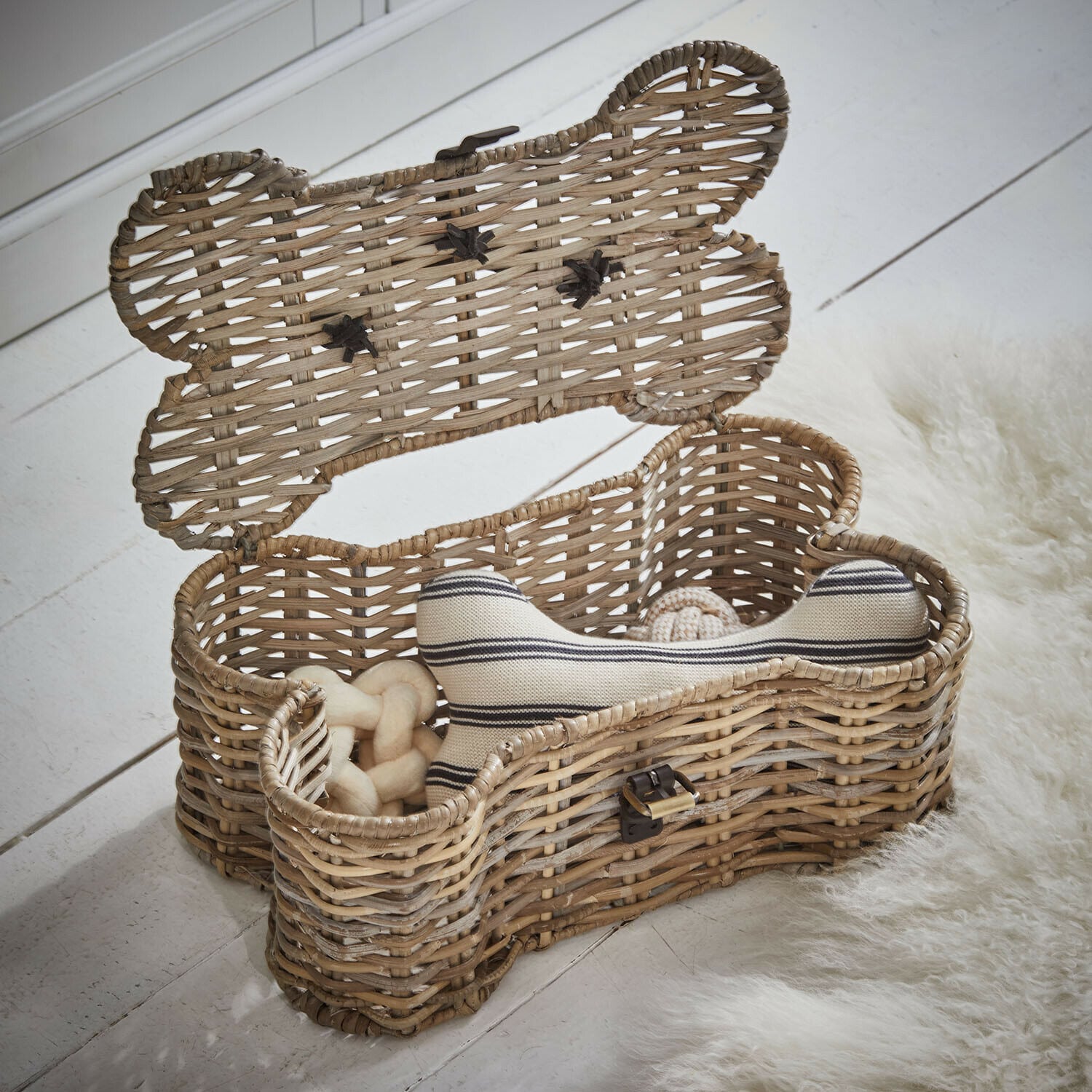 Baule per animali Nuzzlea Cesto in rattan a forma di osso con giocattoli per cani in colore naturale su pavimento bianco