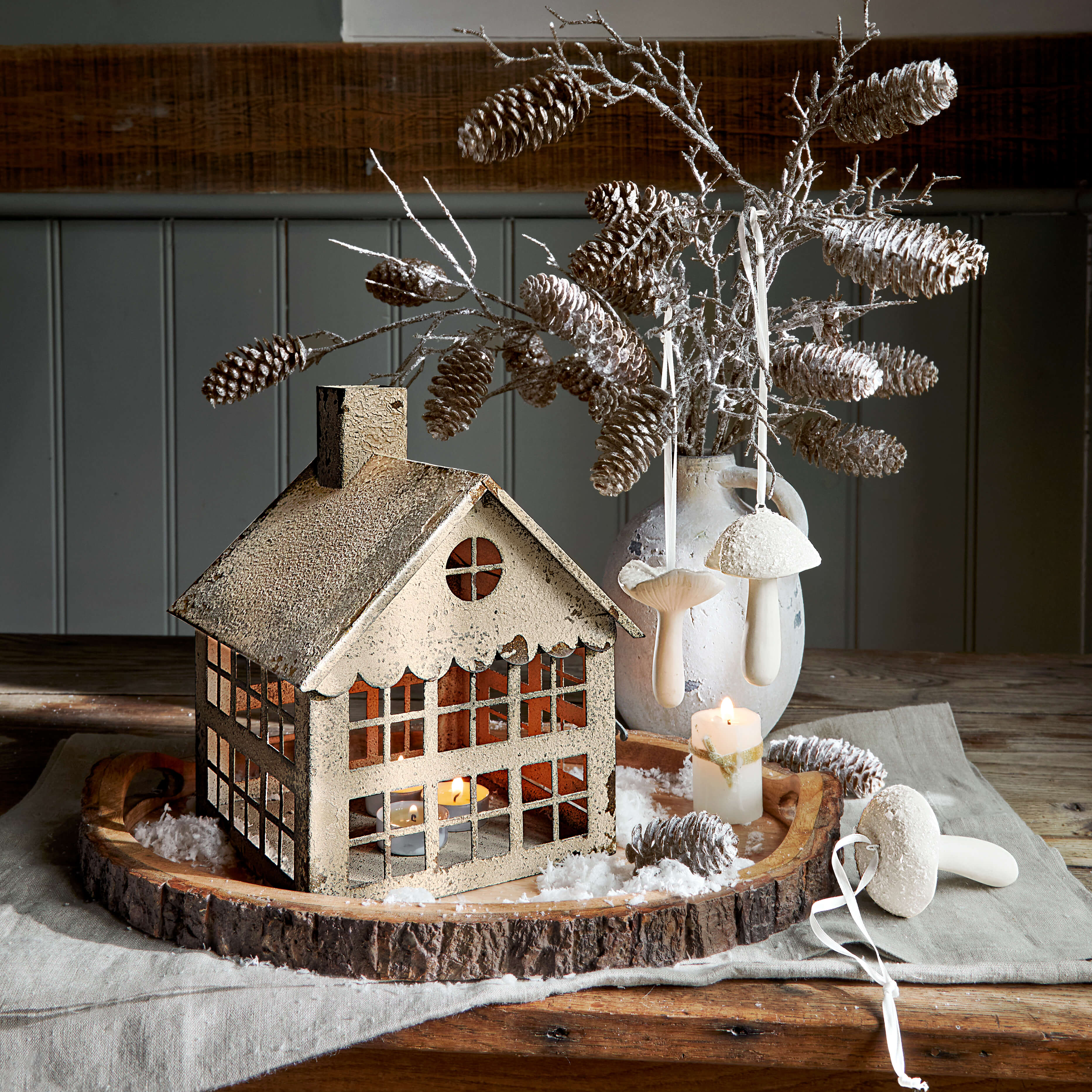 Casetta decorativa in metallo con tealight su base in legno con pigne e funghi bianchi
