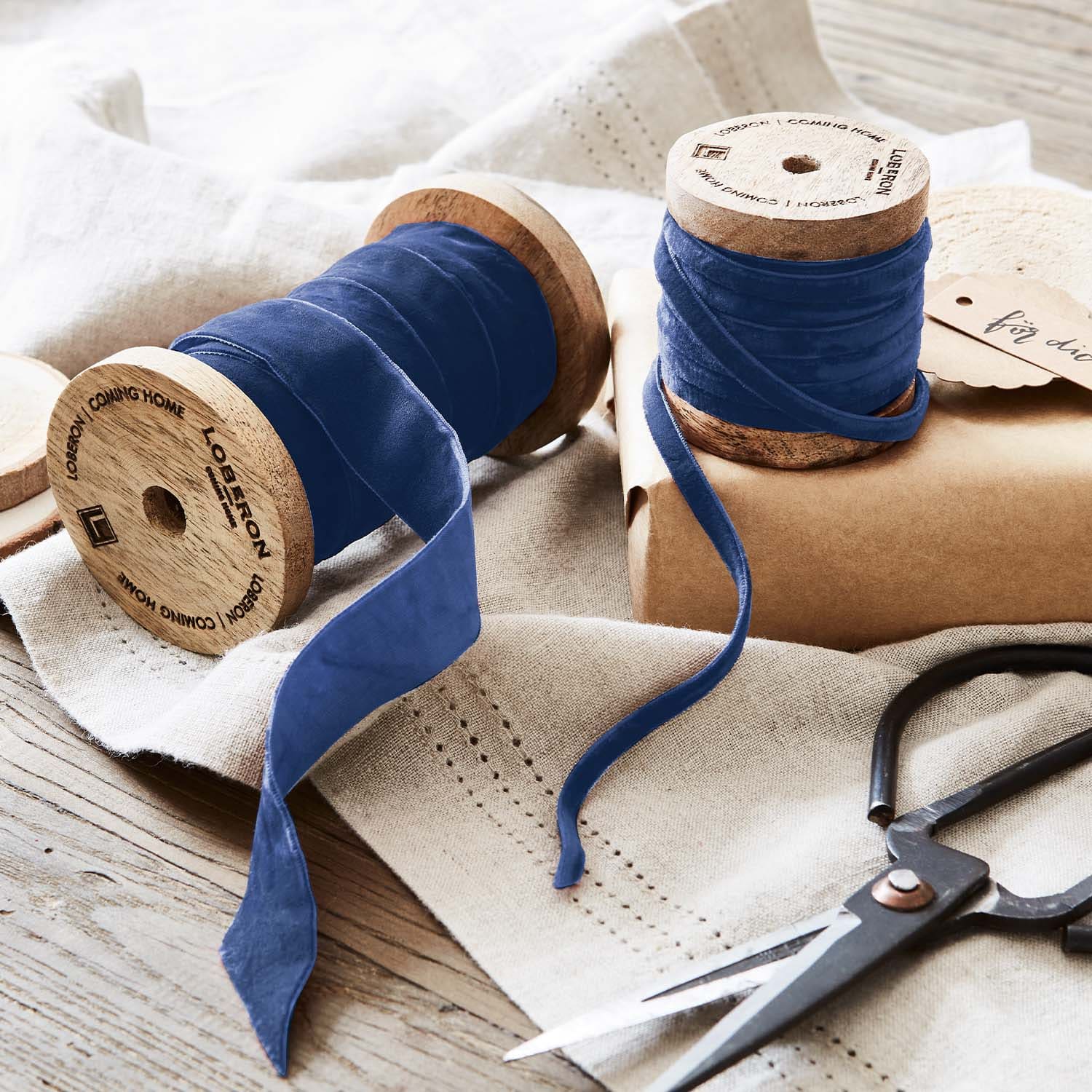 Nastro di velluto blu su bobine di legno con forbici su tessuto di lino per decorazioni e artigianato