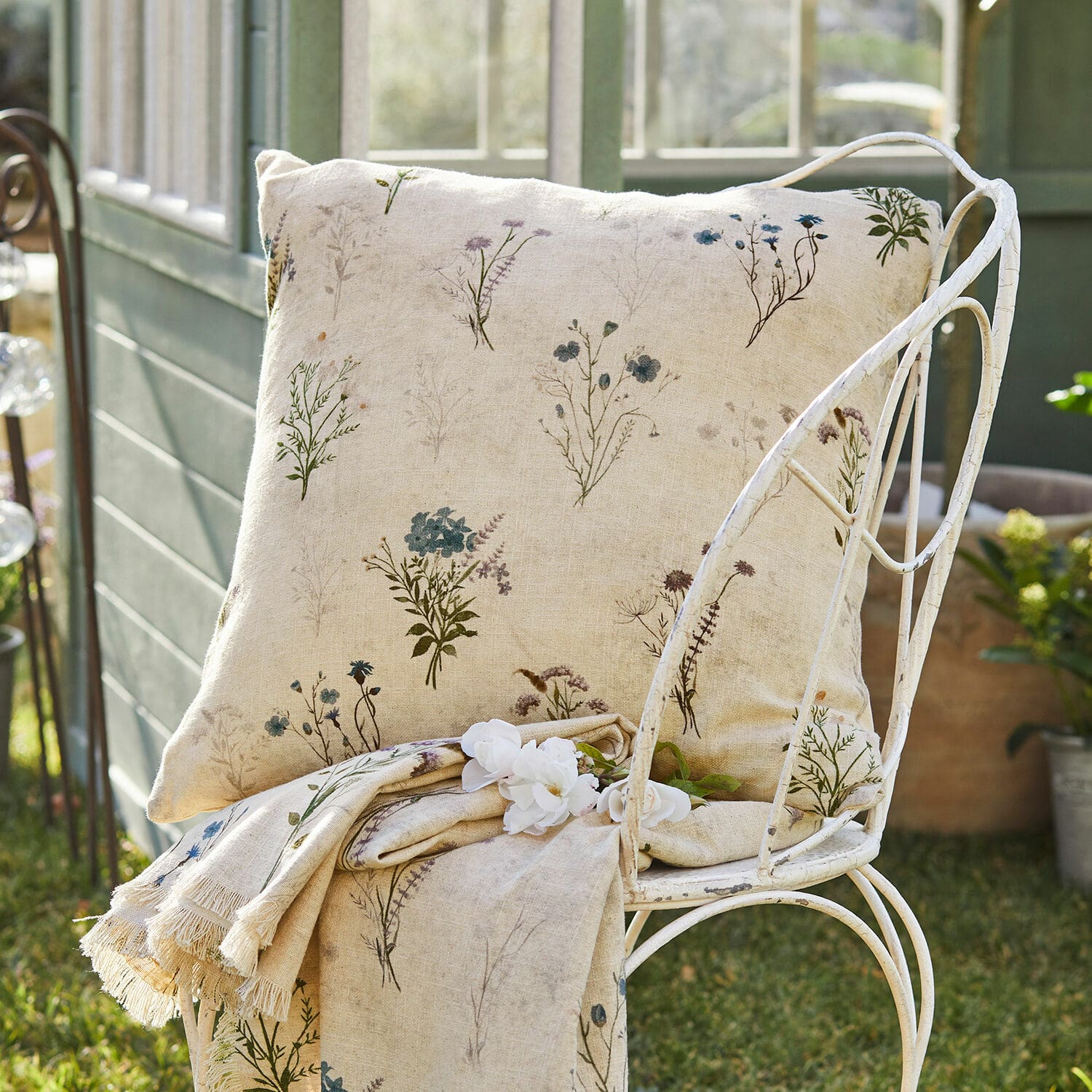 Copricuscino Cabinda Cuscino e coperta in lino beige con delicata fantasia floreale su sedia in metallo in giardino