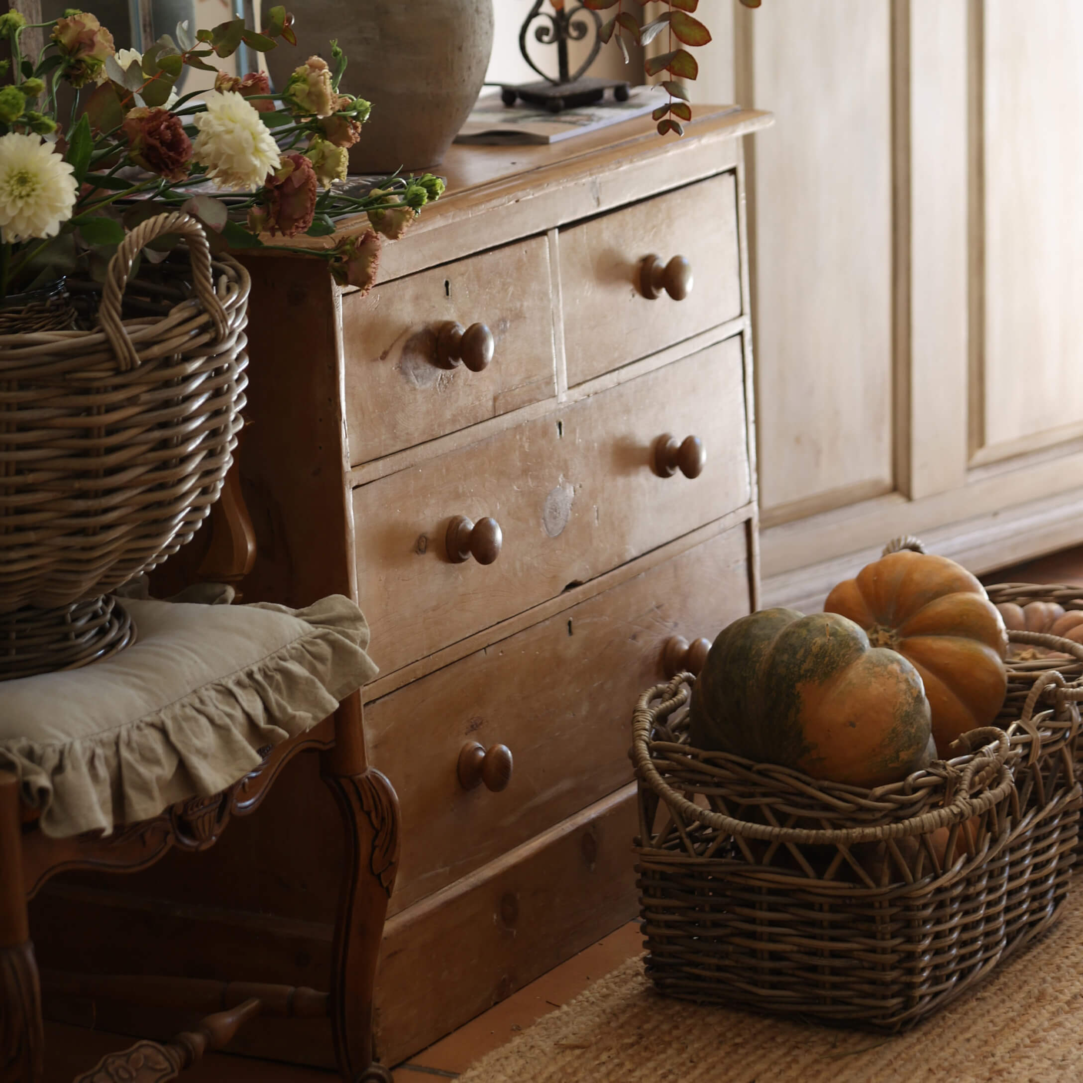 Cassettiera rustica in legno con quattro cassetti e cesta di vimini con zucche in ambiente accogliente