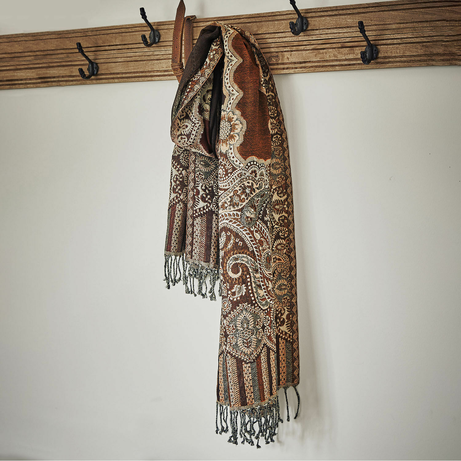 Scialle Crédin Sciarpa marrone decorata con frange appesa a appendiabiti in legno su parete bianca