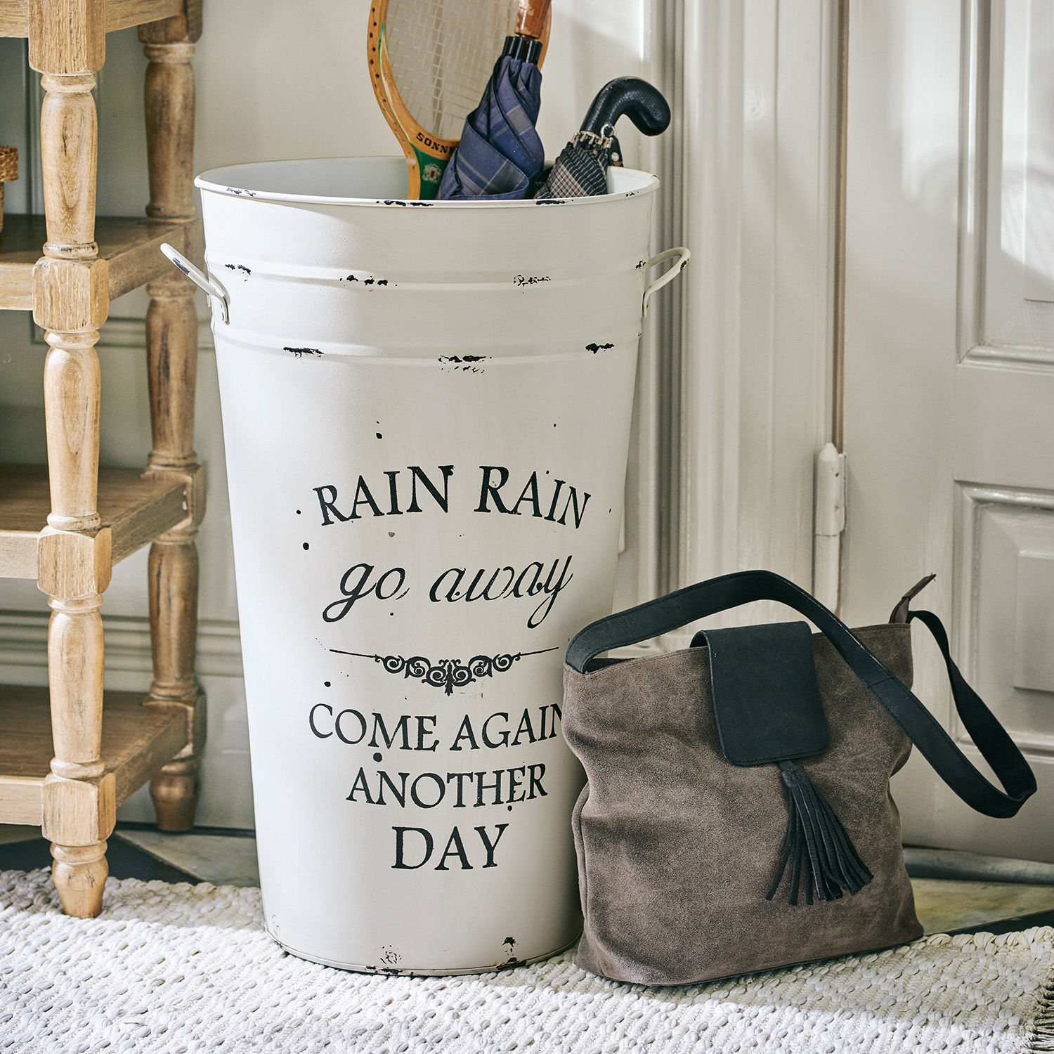 Portaombrelli Rain Portaombrelli in metallo bianco con scritta e borsa in camoscio marrone sul pavimento vicino alla porta