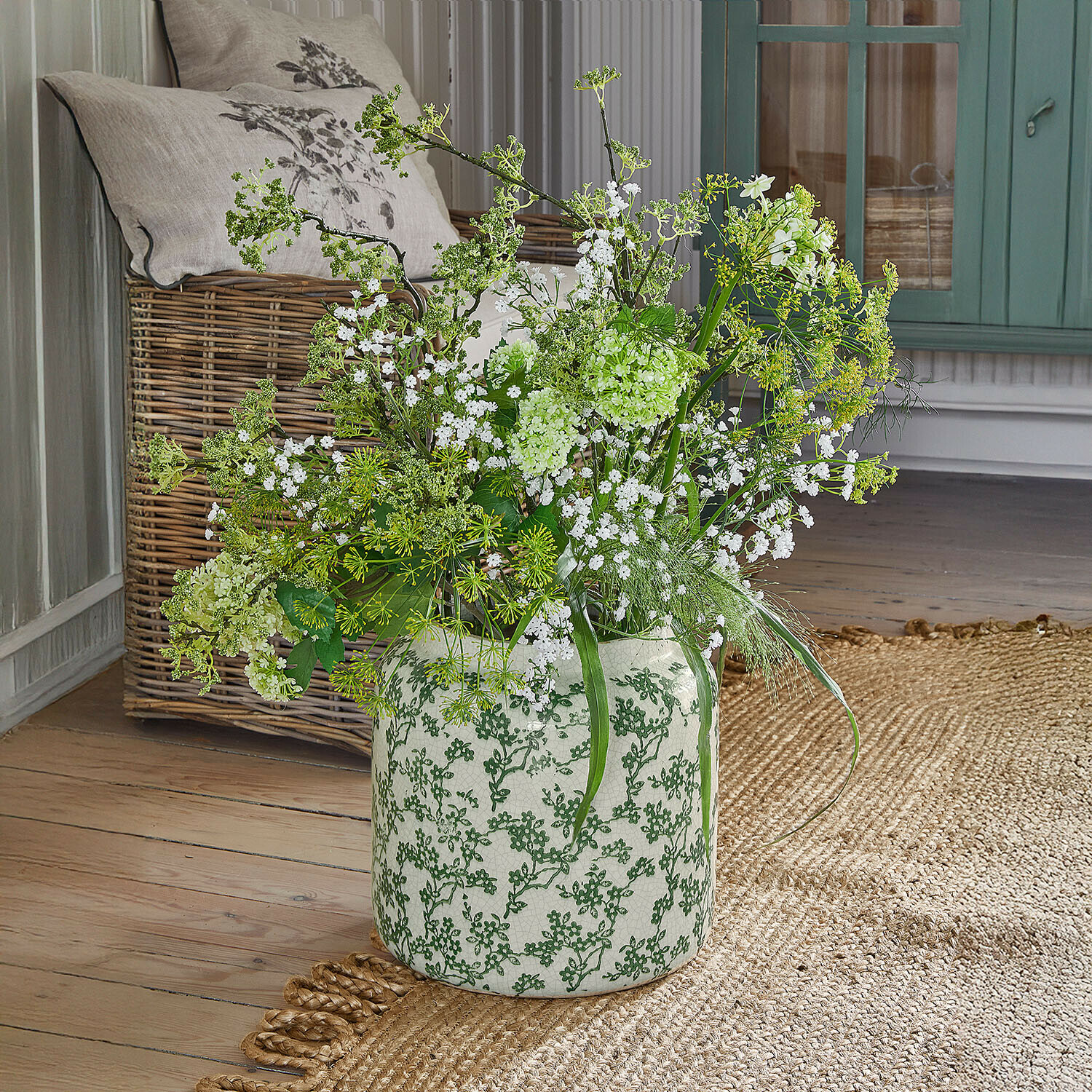 Vaso Vaudrisse Vaso in ceramica bianca con motivo verde, fiori bianchi e rami verdi su pavimento in legno