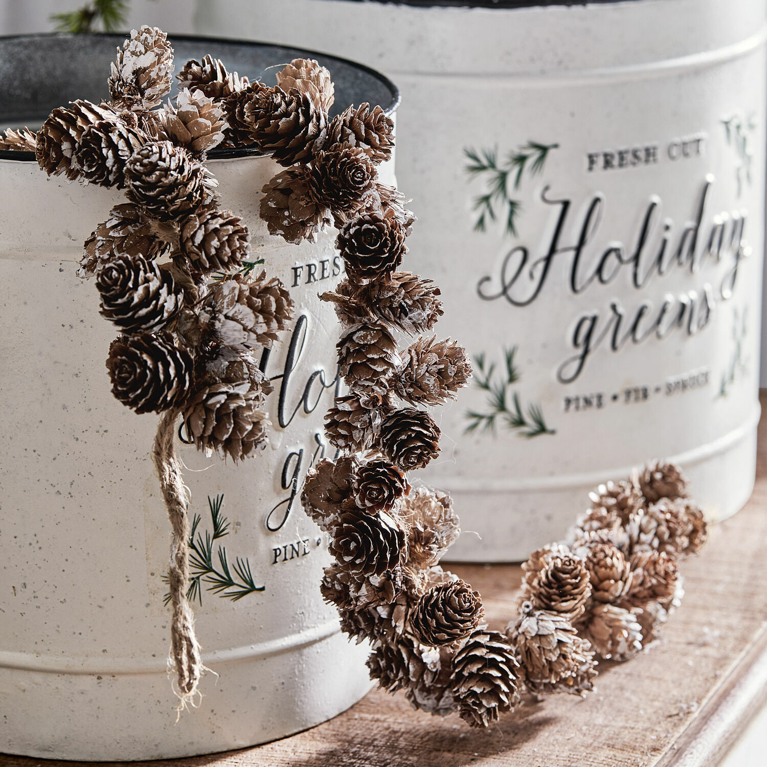 Ghirlanda di abete Jacci Corona decorativa di pigne marroni naturali con accenti bianchi davanti a contenitori metallici bianchi