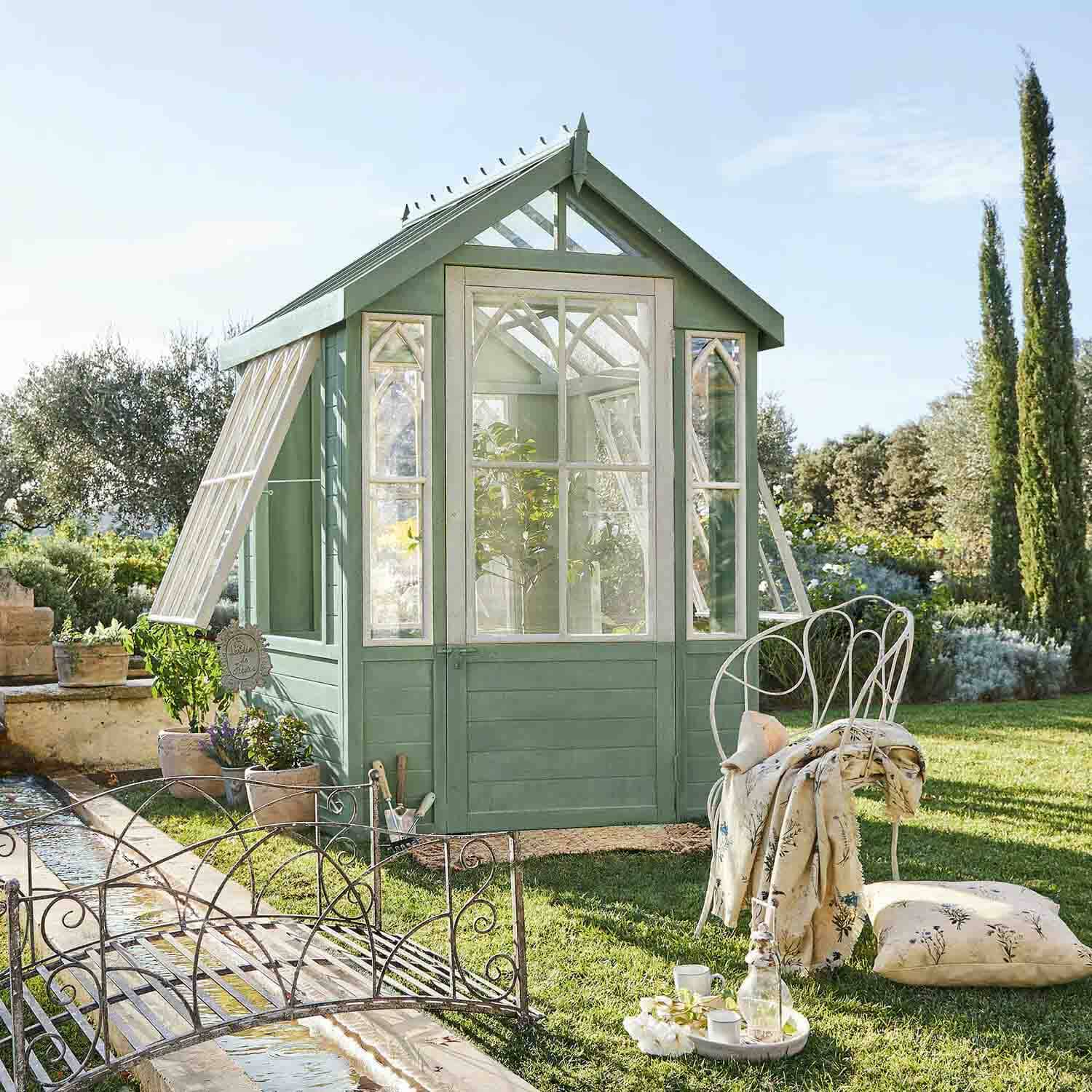 Serra in legno verde con cornici bianche nel giardino, sedia in metallo con cuscino accanto