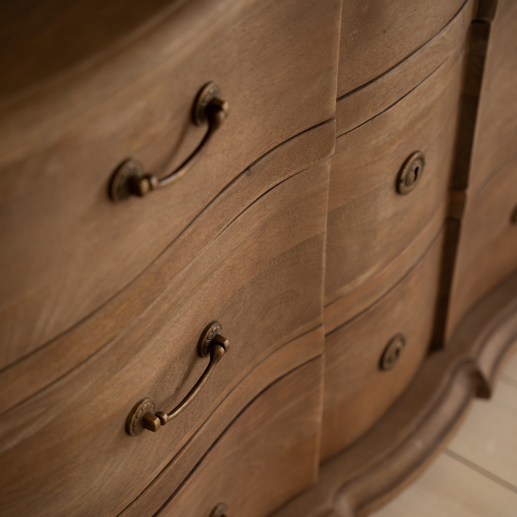 Primo piano di una cassettiera in legno con maniglie decorative in ottone e finitura naturale del legno