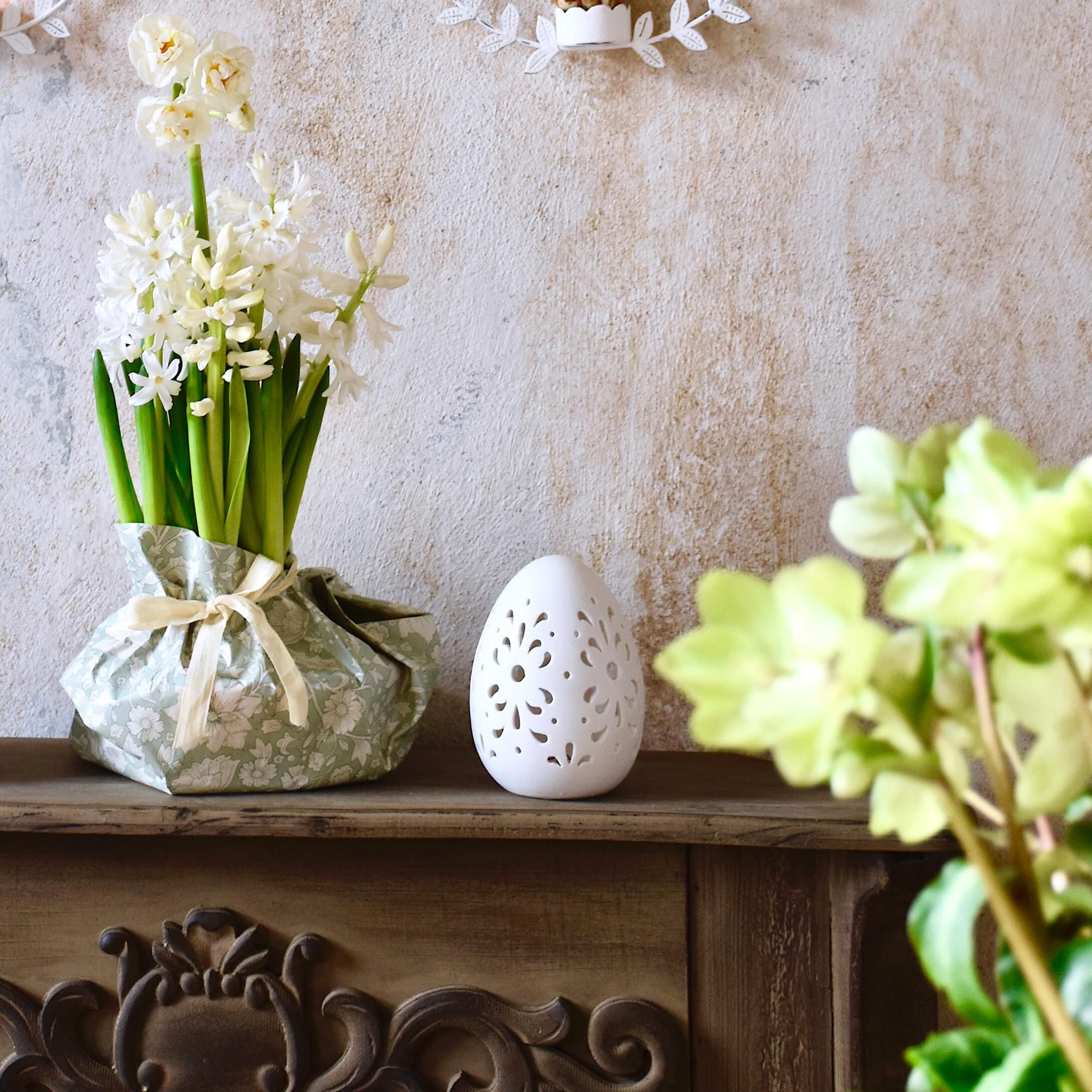 Fiori bianchi in confezione decorativa verde e decorazione a forma di uovo in ceramica bianca su mensola in legno