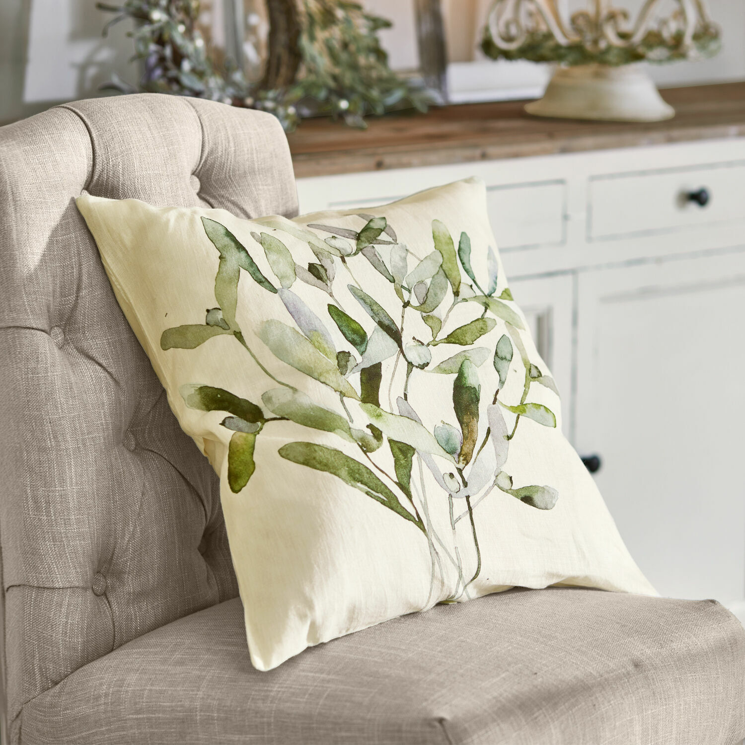 Copricuscino Mistletoe Cuscino beige con motivo foglie verdi su sedia grigia in stile naturale
