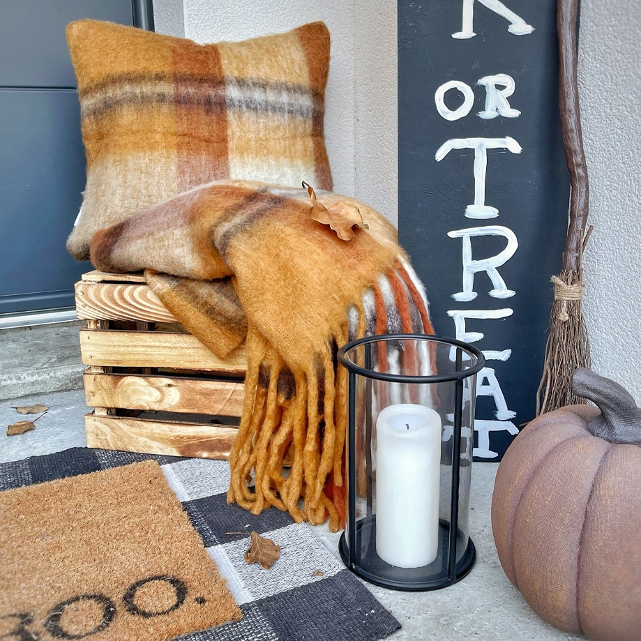 Plaid e cuscino morbidi arancione e marrone con frange su cassa di legno all'ingresso