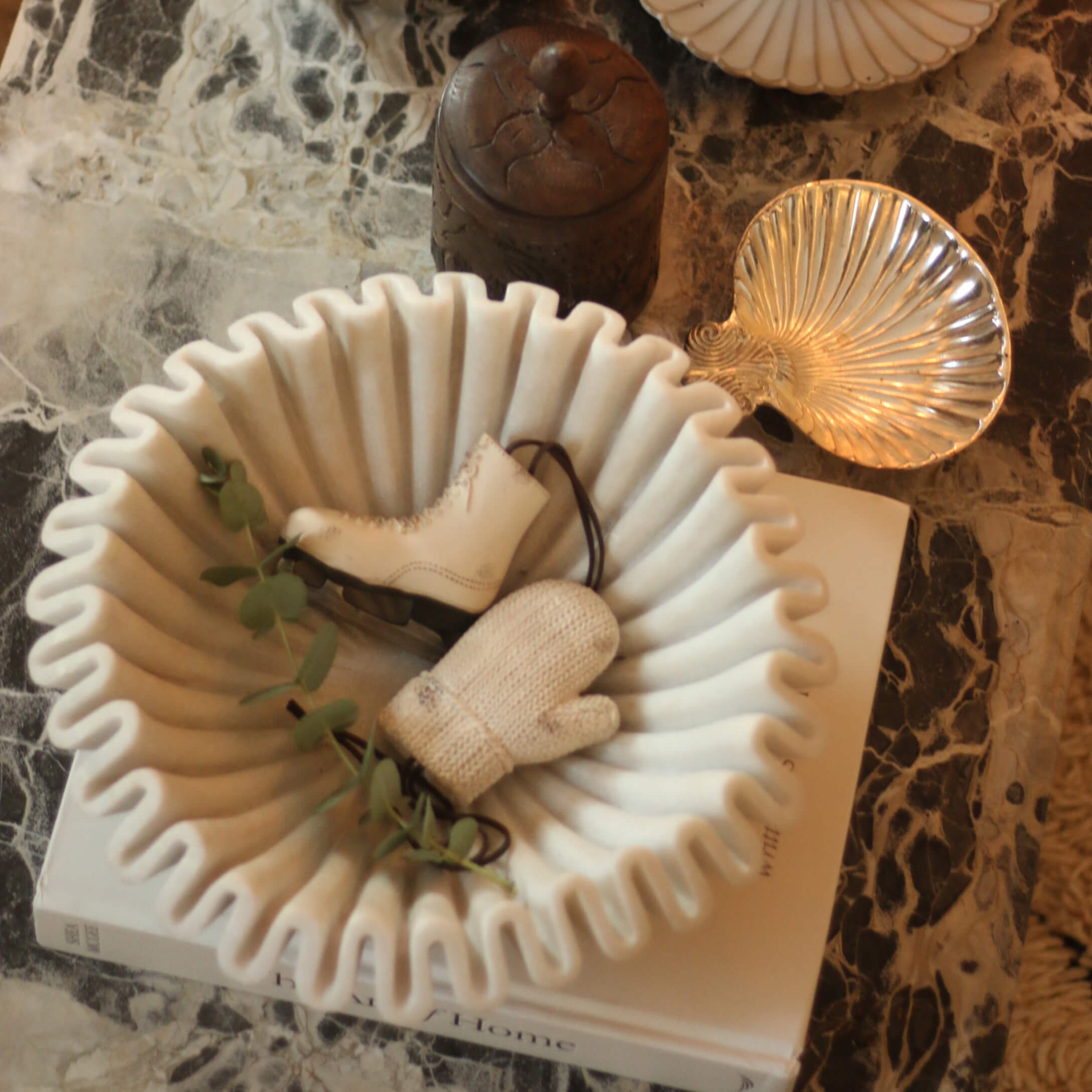 Ciotola in ceramica bianca con bordo ondulato decorata con pattino e guanto su tavolo in marmo