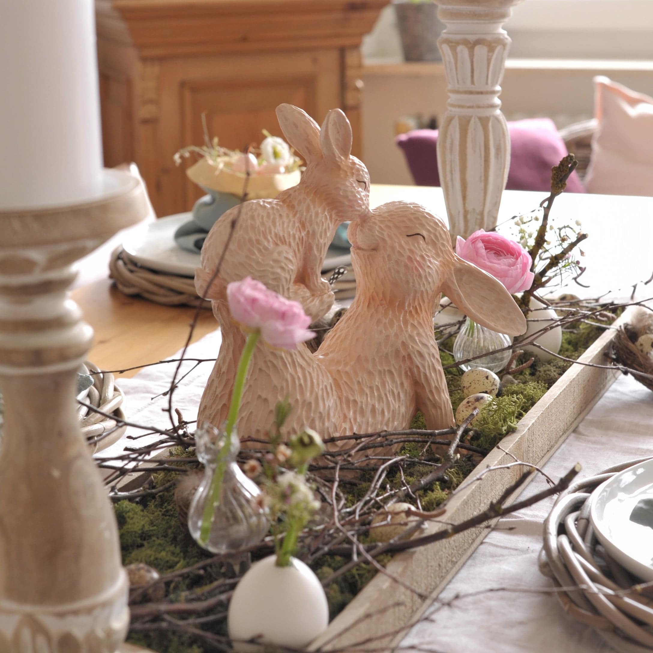 Decorazione da tavolo con conigli in ceramica beige e fiori rosa su muschio verde