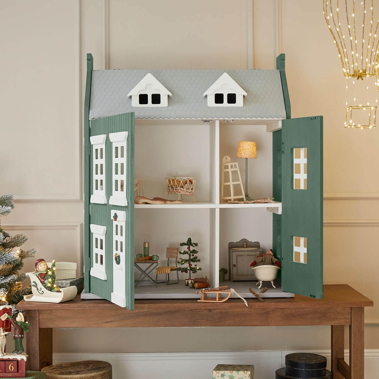 Casa delle bambole in legno verde e grigia con porte aperte e decorazioni natalizie all'interno