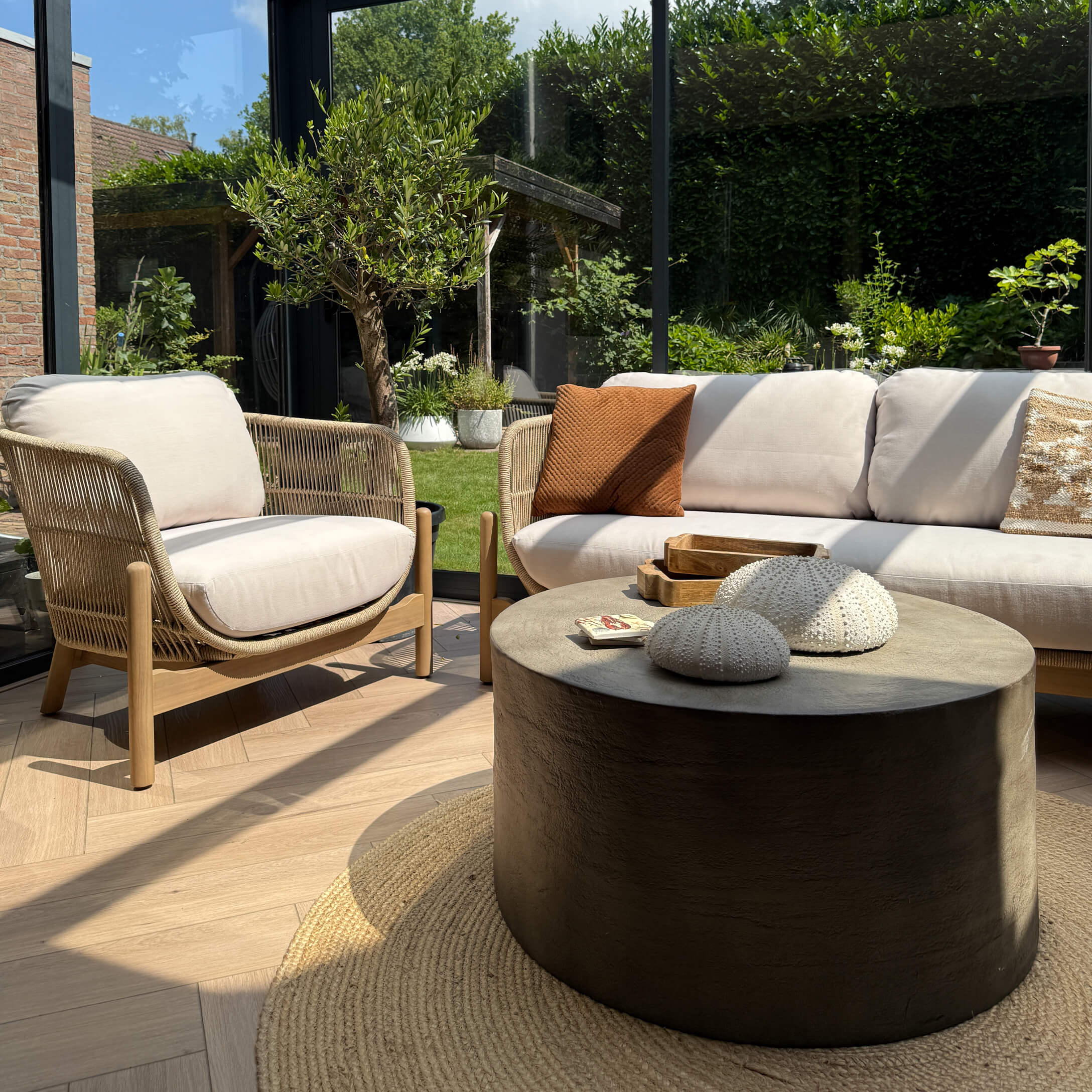 Soggiorno moderno con divano beige, poltrona in legno e tessuto, tavolino rotondo nero e decorazioni naturali