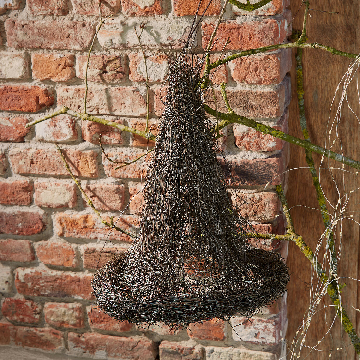 Cappello decorativo Talmora Decorazione sospesa in filo nero a forma di cappello da strega davanti a muro di mattoni
