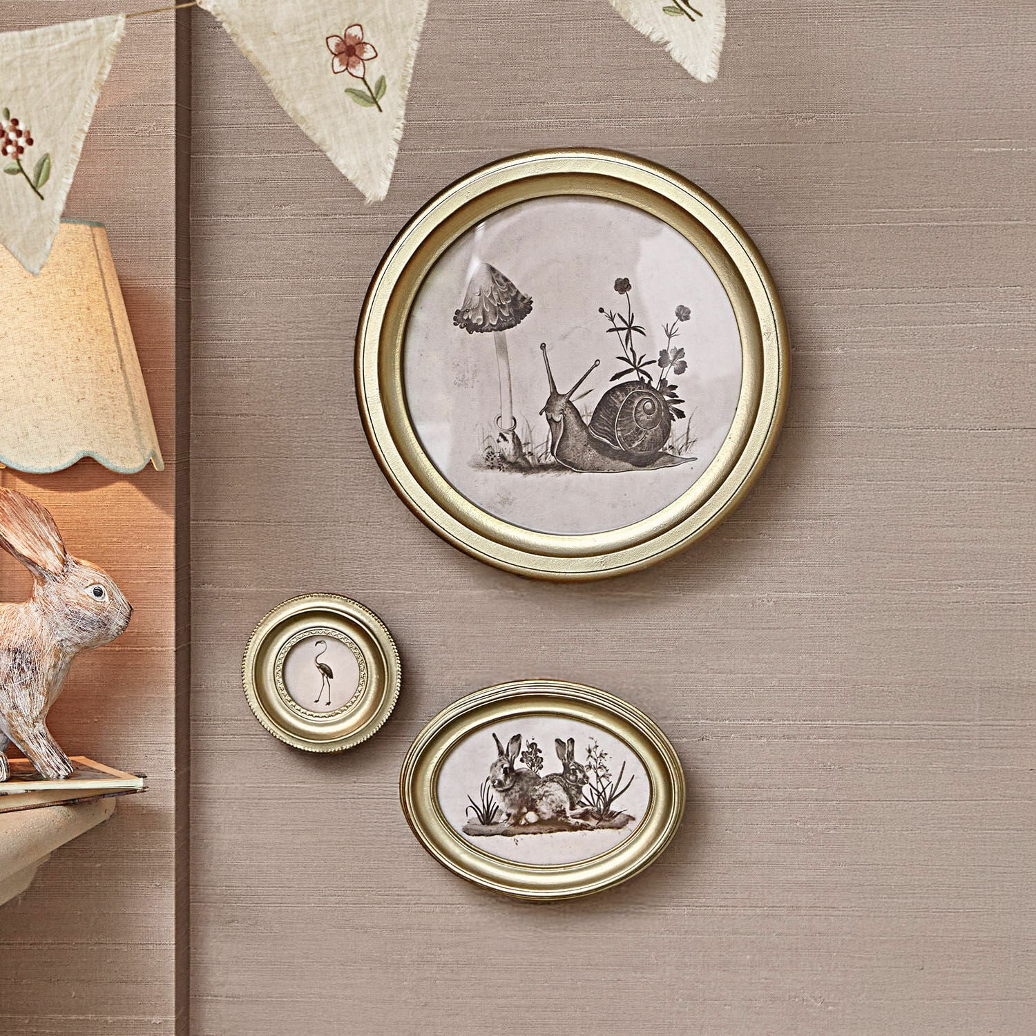 Set di 3 quadretti Atriana Set di tre cornici dorate con illustrazioni in bianco e nero di animali e piante su parete beige.
