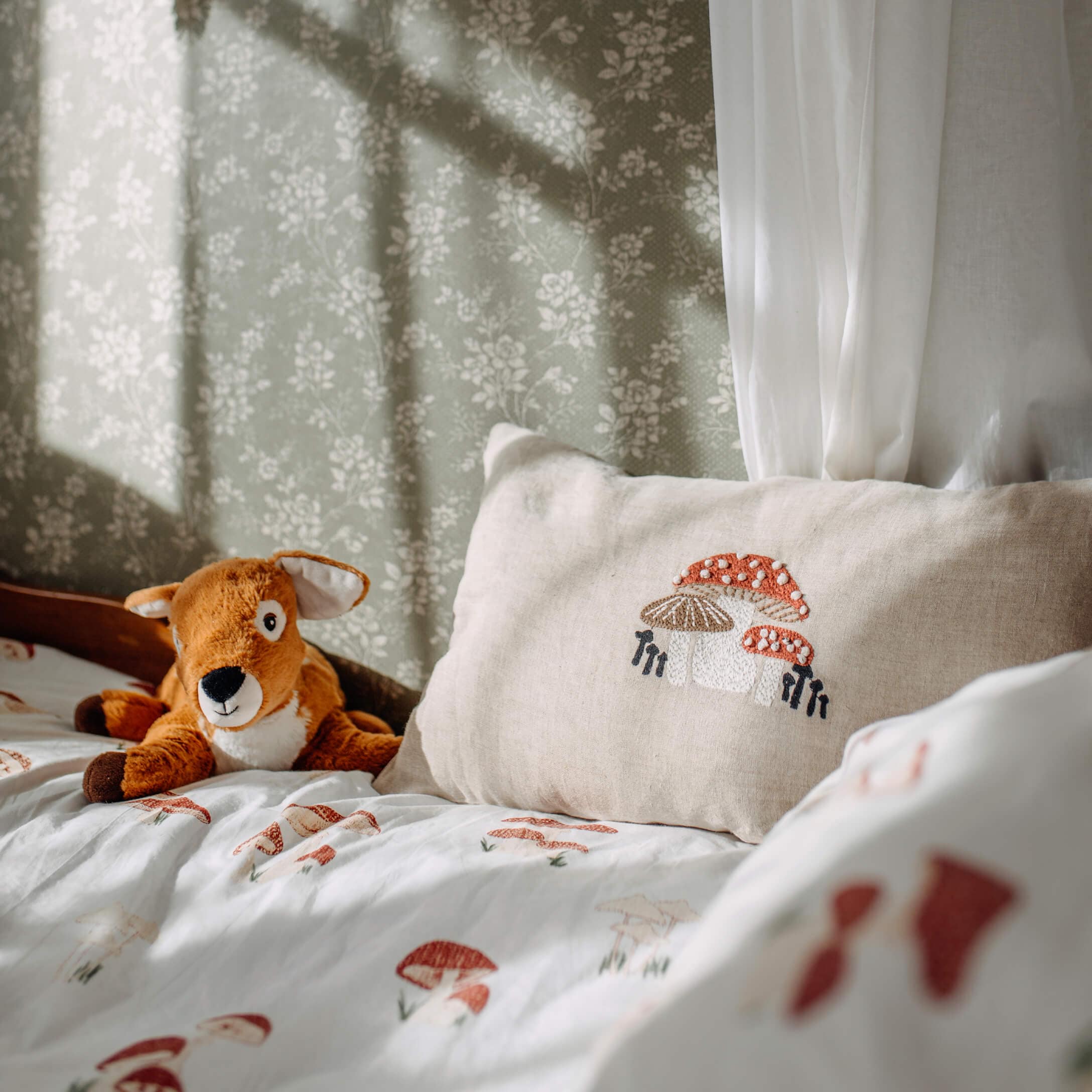 Cuscino in lino beige con ricamo di funghi su letto con biancheria da letto a tema funghi e peluche di cervo