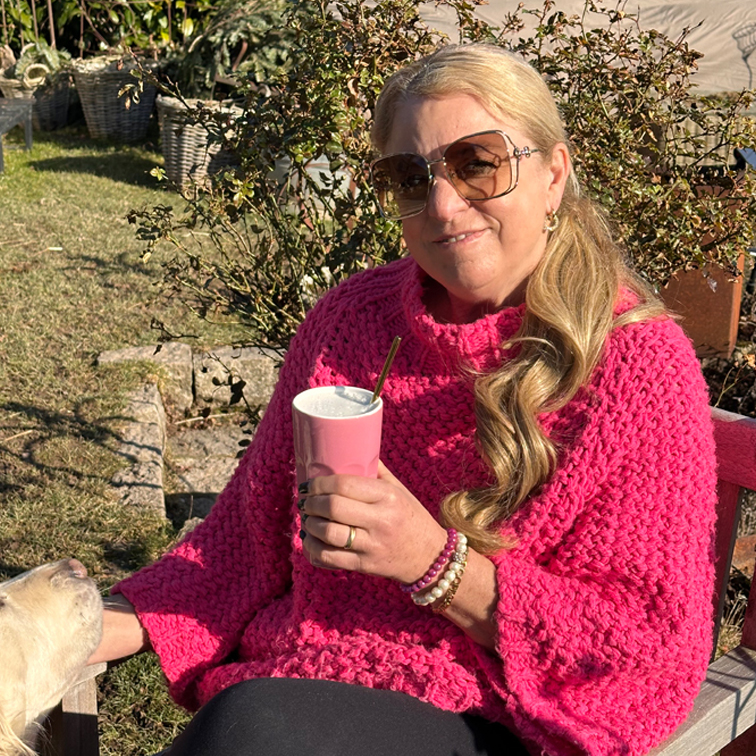 Donna con maglione spesso rosa che tiene una tazza rosa all'aperto in una giornata di sole con cane accanto