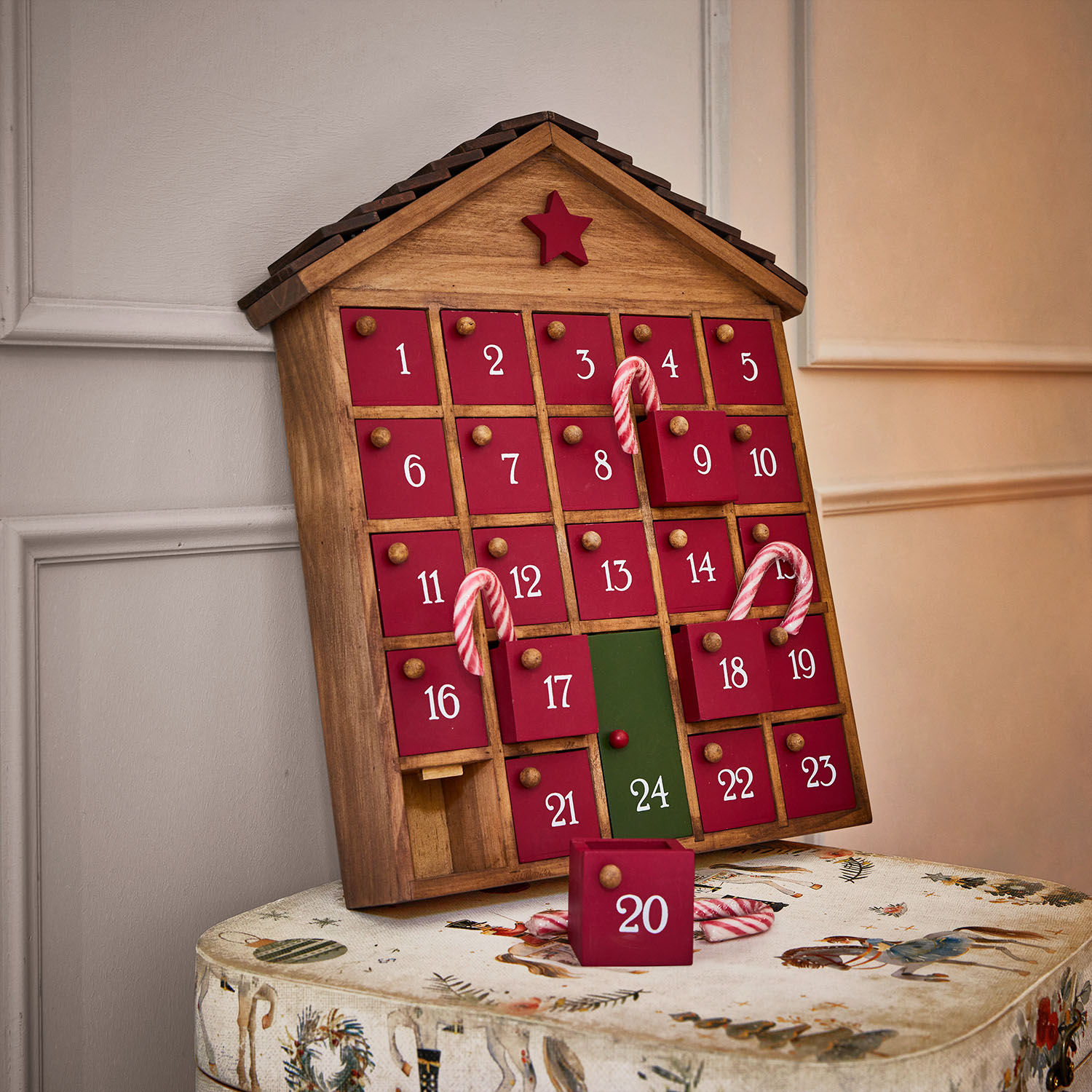 Calendario dell'Avvento in legno a forma di casa con sportelli rossi e numero 24 verde, decorato con bastoncini di zucchero