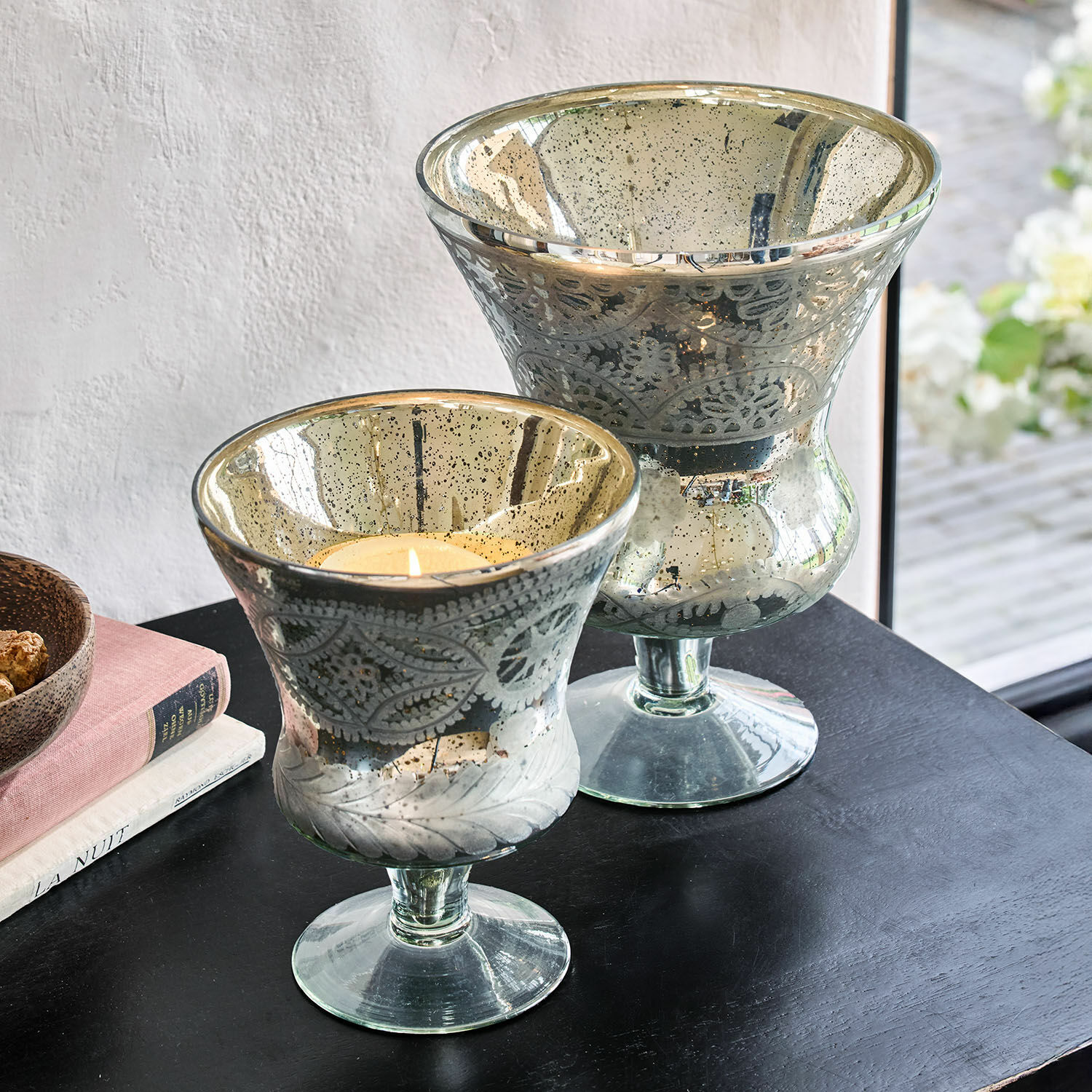 Coppia di lanterne Zorayne Due portacandele decorativi in vetro con motivo a foglie e finitura argentata su tavolo nero