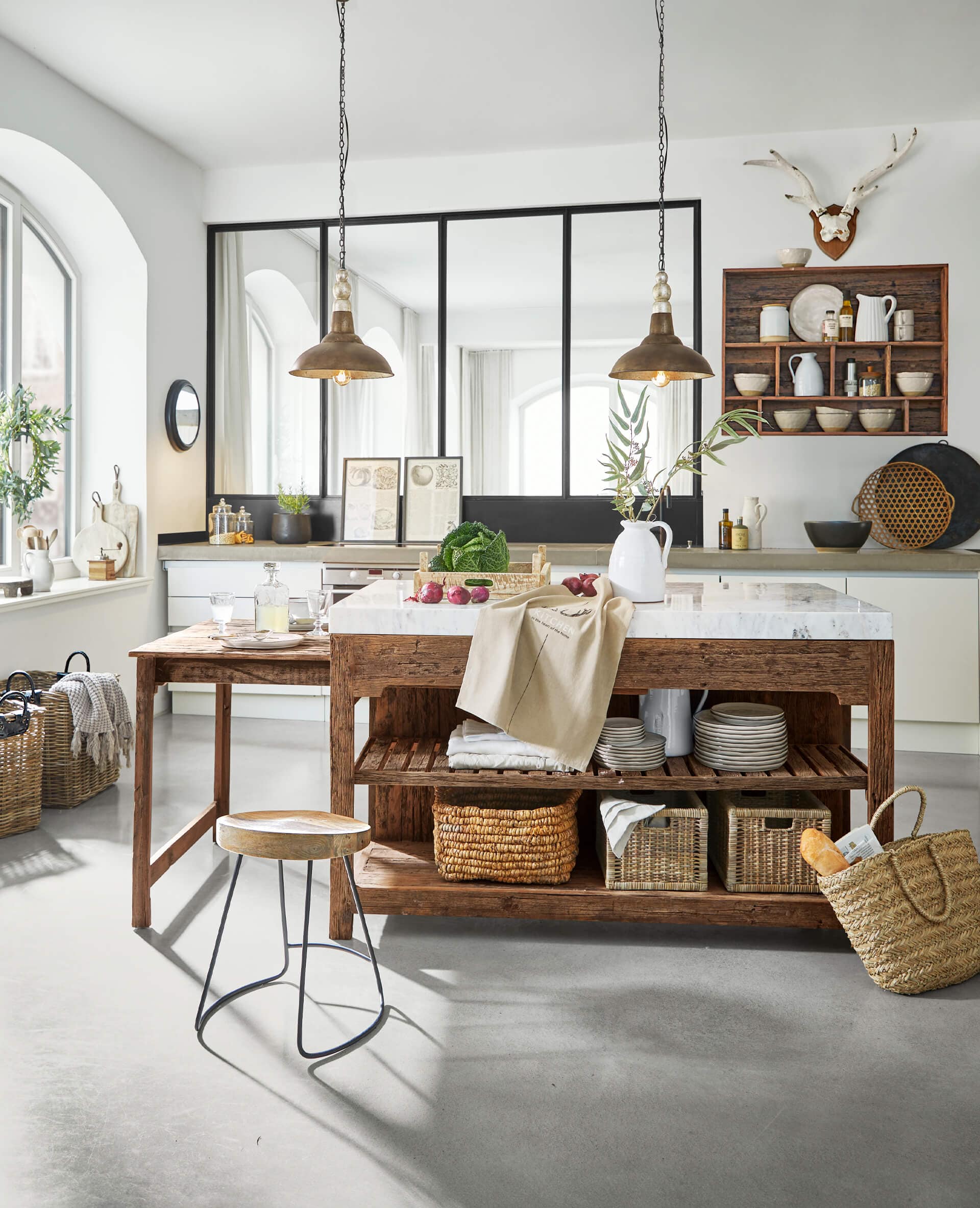 Cucina rustica con isola in legno e piano in marmo, cesti naturali e lampade a sospensione