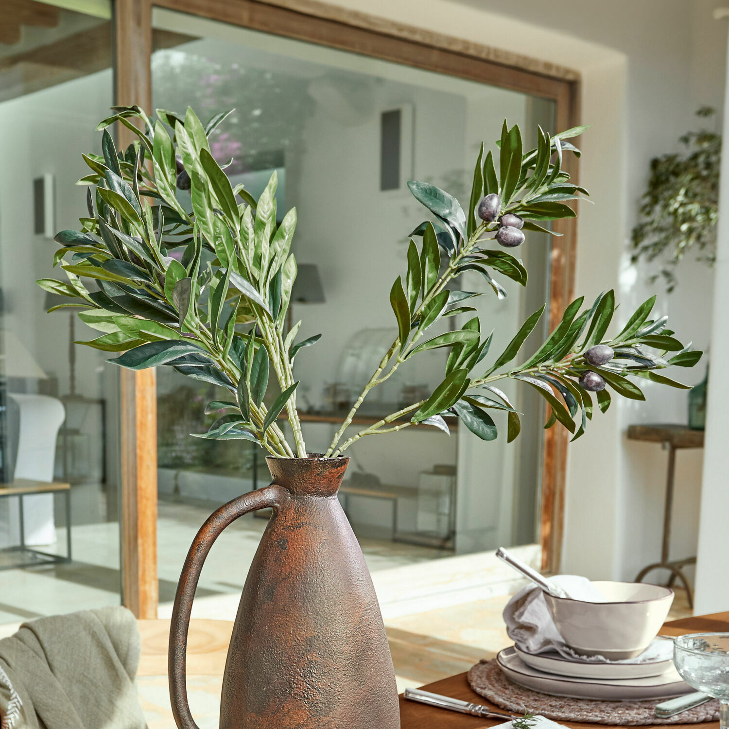 Coppia di rametti d’ulivo decorativi Olives Brocca rustica in metallo color ruggine con rami verdi di ulivo su tavolo da pranzo