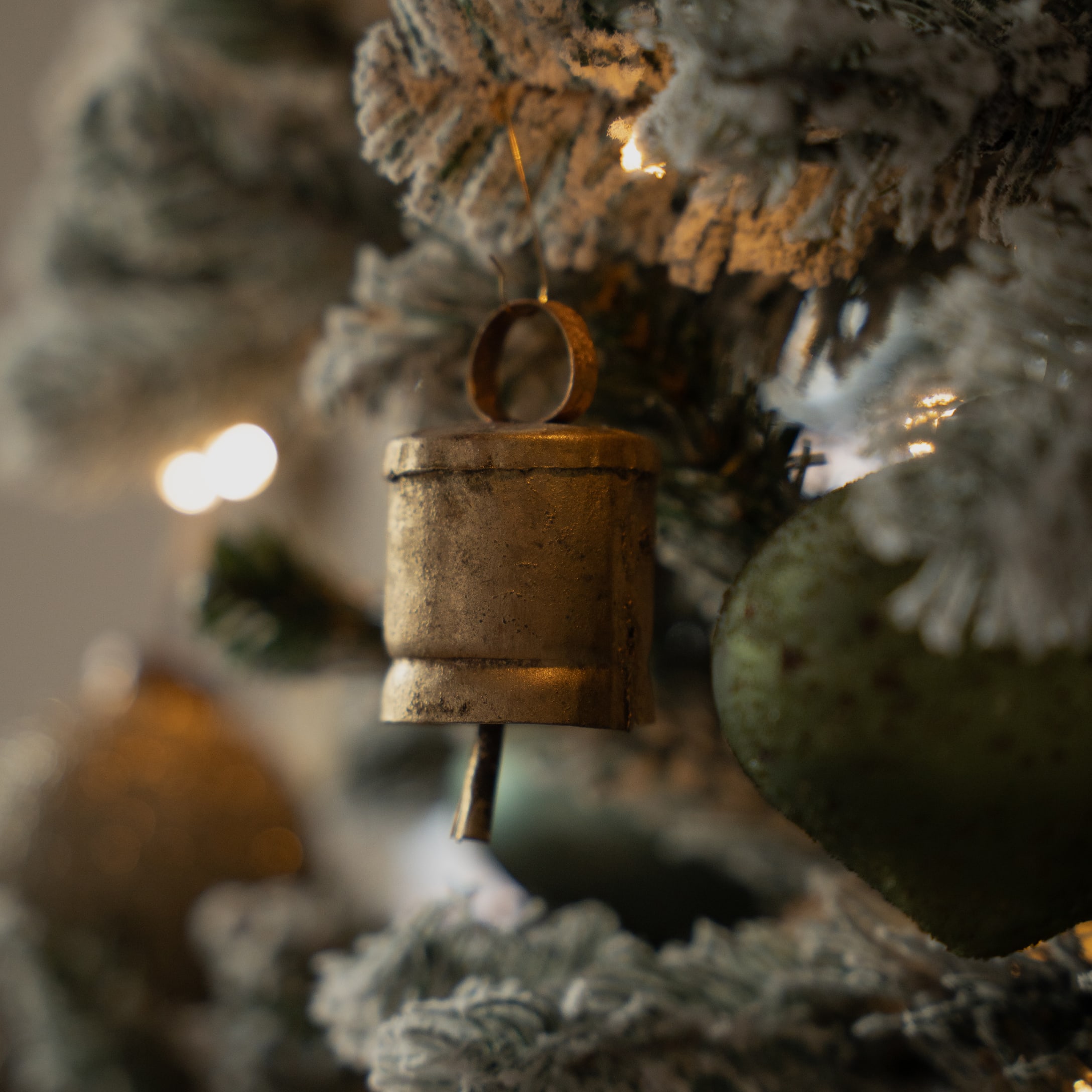 Campanella metallica dorata appesa a un albero di Natale innevato con luci decorative