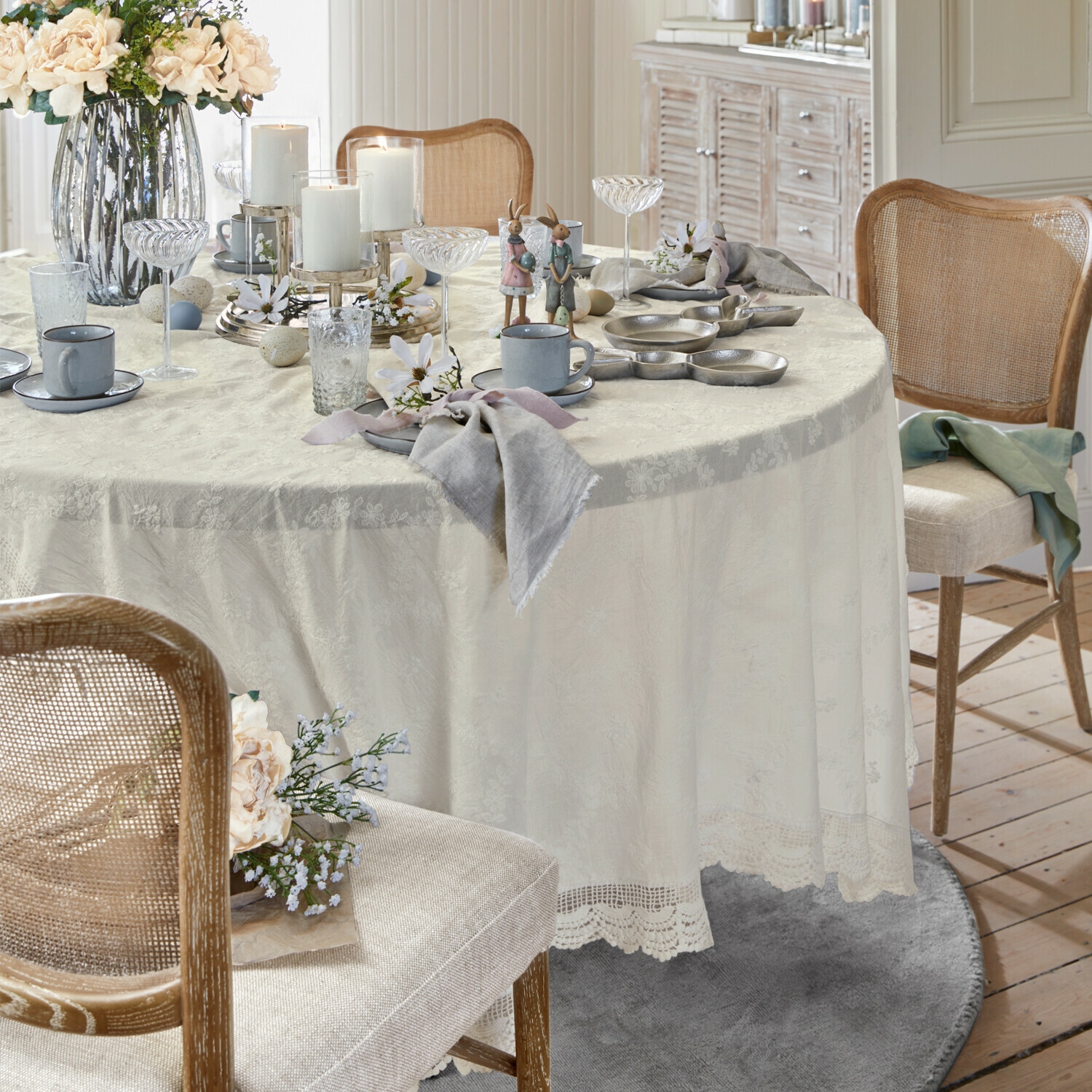 Tavolo elegante con tovaglia crema in pizzo, decorazioni pasquali e servizio da caffè grigio