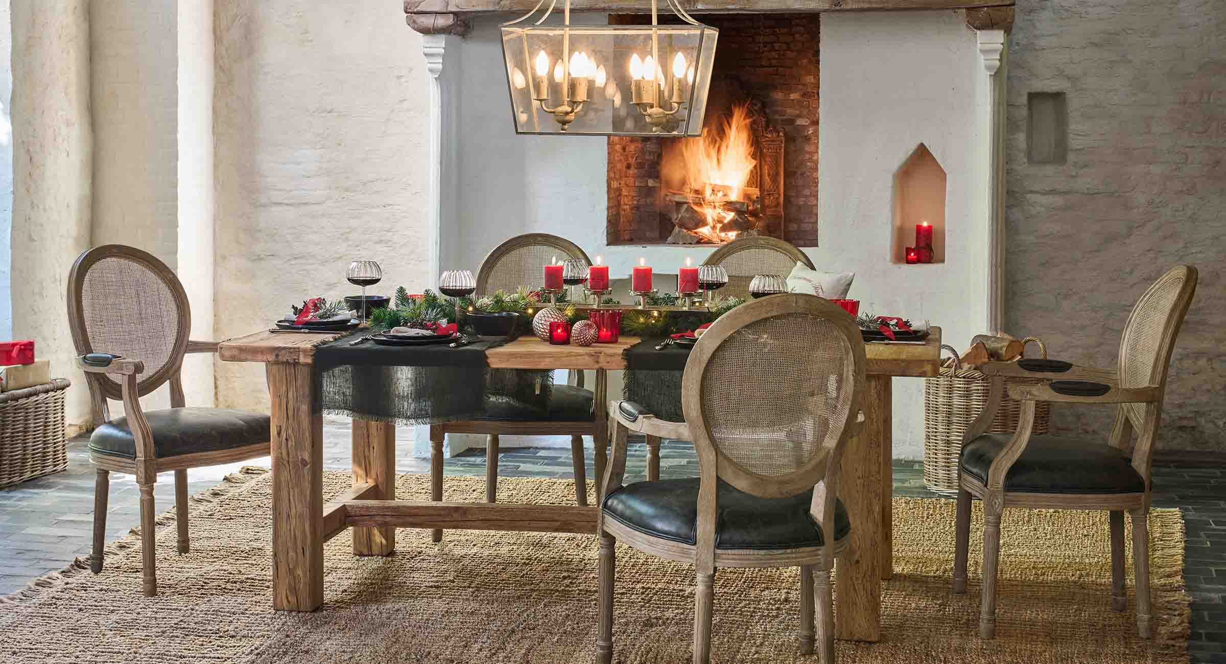 Tavolo rustico in legno con decorazioni naturali e candele rosse vicino a un camino acceso