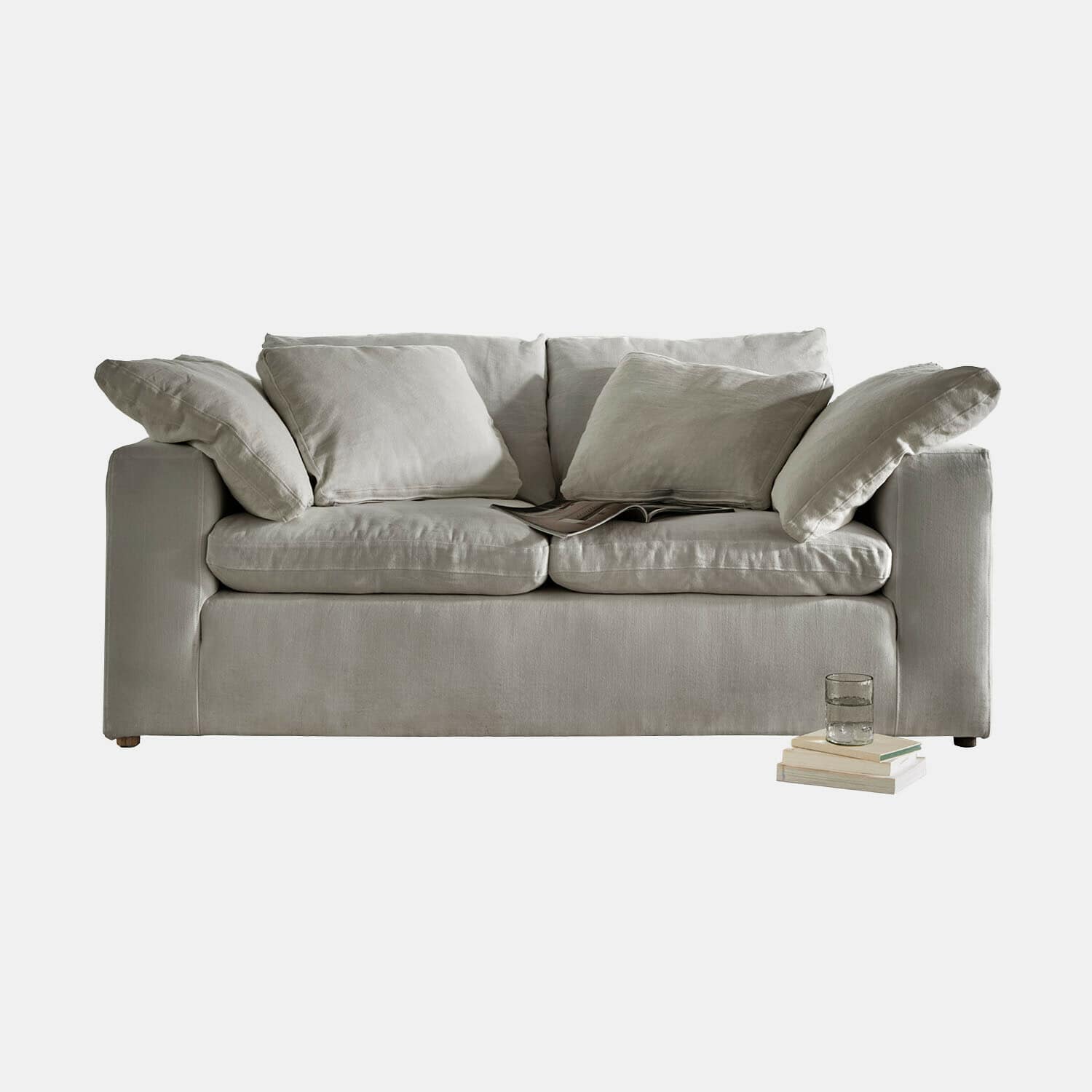 Divano Everholt Divano beige in tessuto morbido con cuscini e libri accanto, arredo confortevole per soggiorno