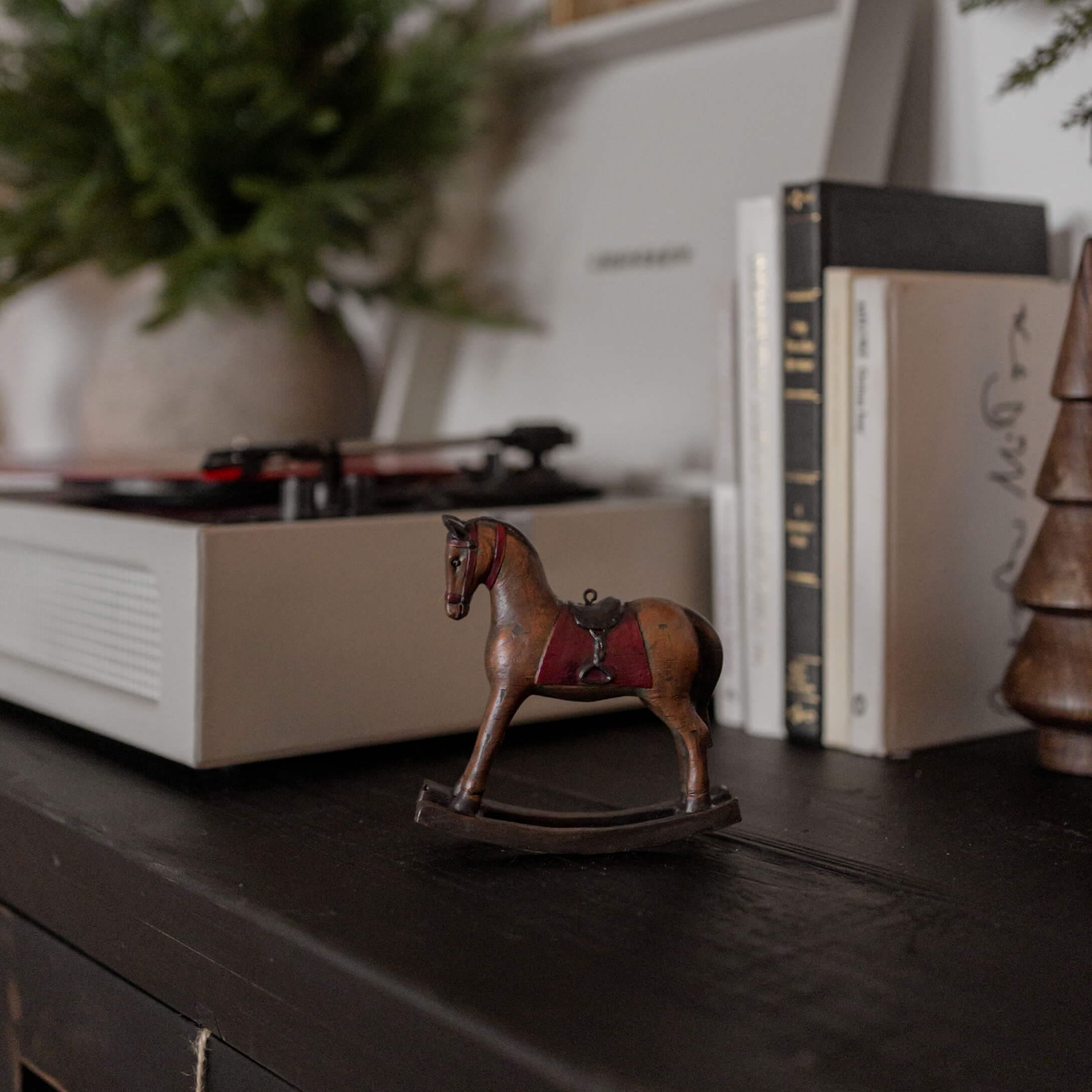 Cavallo a dondolo in legno marrone con sella rossa su superficie nera vicino a libri e giradischi