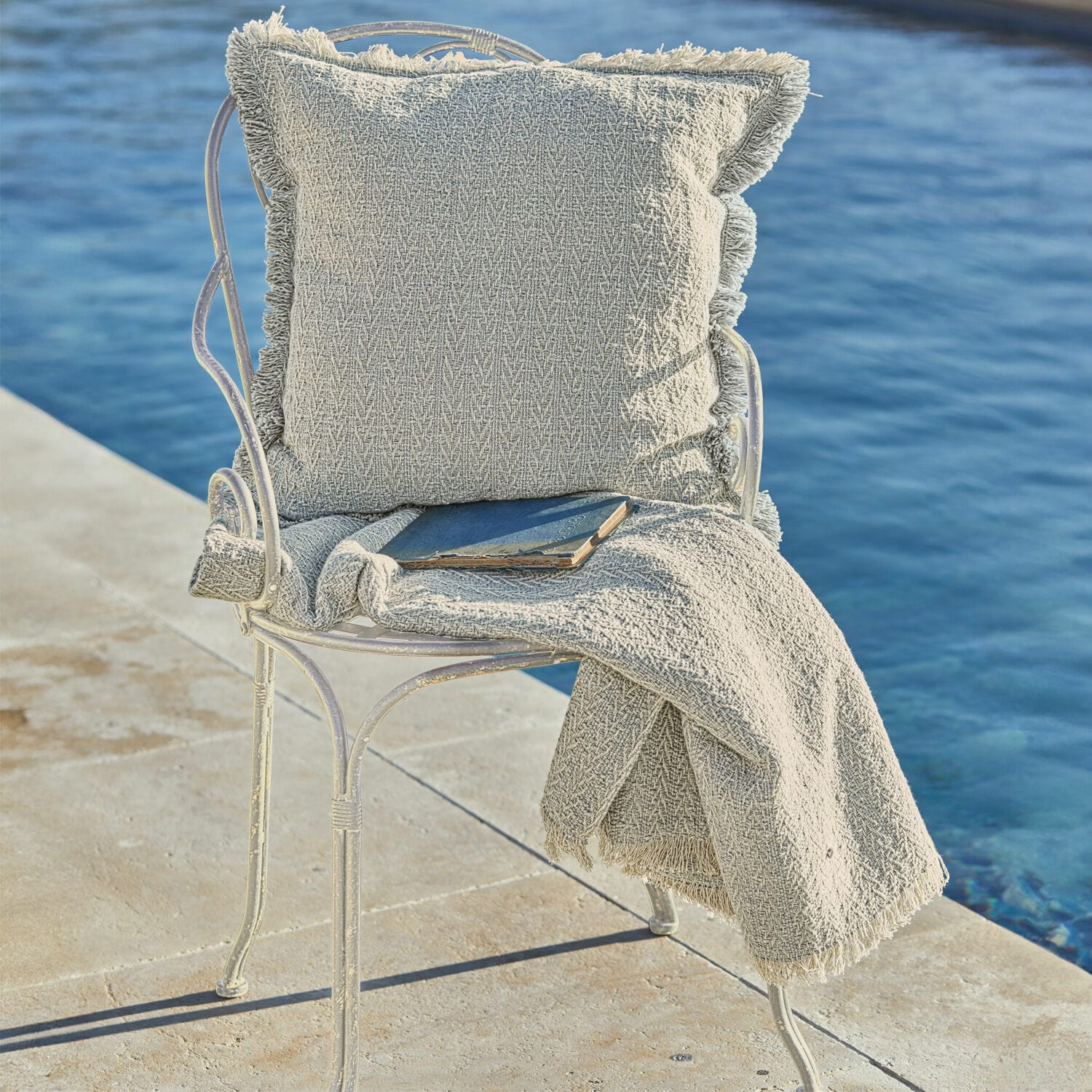 Sedia Aube Cuscino beige e coperta con frange su sedia in metallo vicino all'acqua, decorazione per interni ed esterni