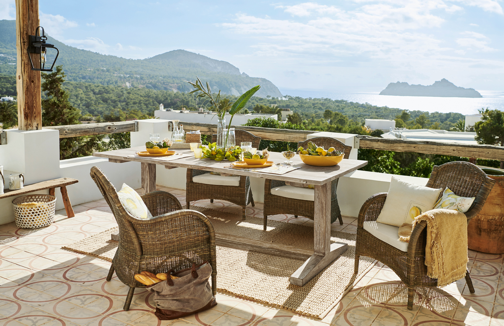 Terrazza con mobili in rattan e tavolo in legno chiaro con vista mare e monti, stile mediterraneo