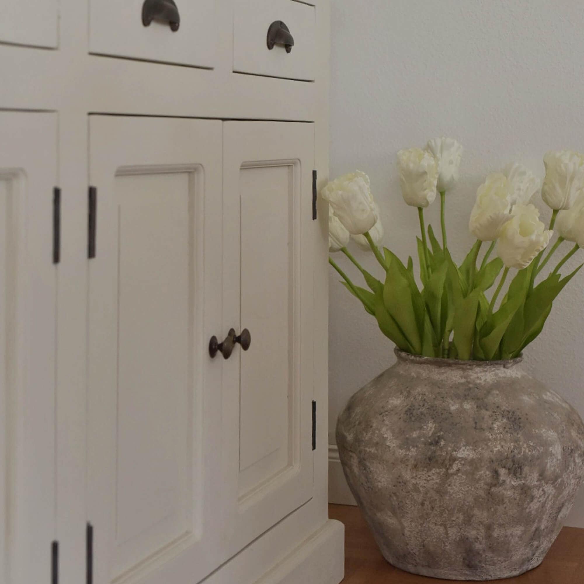 Grande vaso in ceramica grigia con tulipani bianchi accanto a un armadio in legno bianco