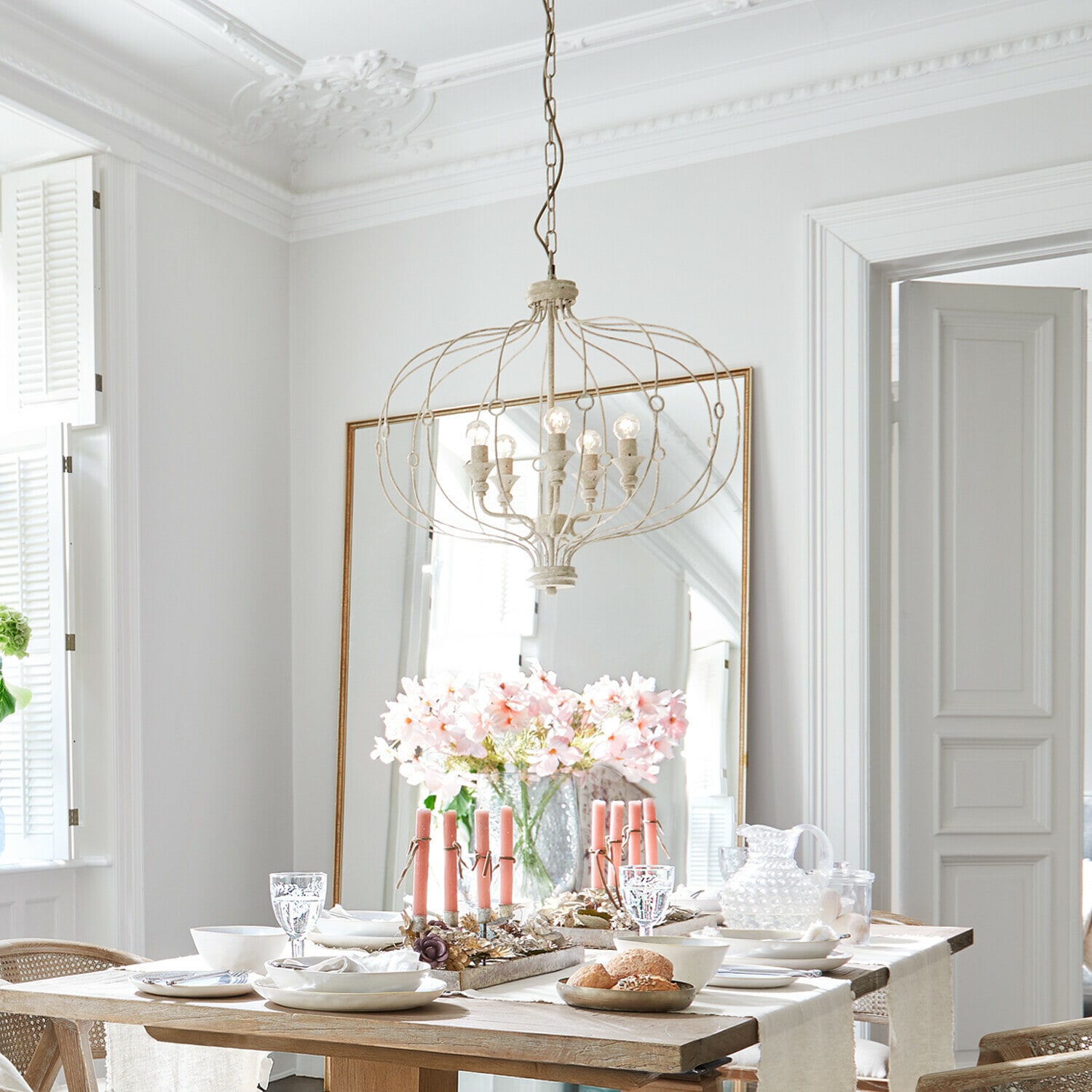 Lampadario Aragonese Sala da pranzo luminosa con tavolo in legno, candele rosa e lampadario metallico vintage sospeso