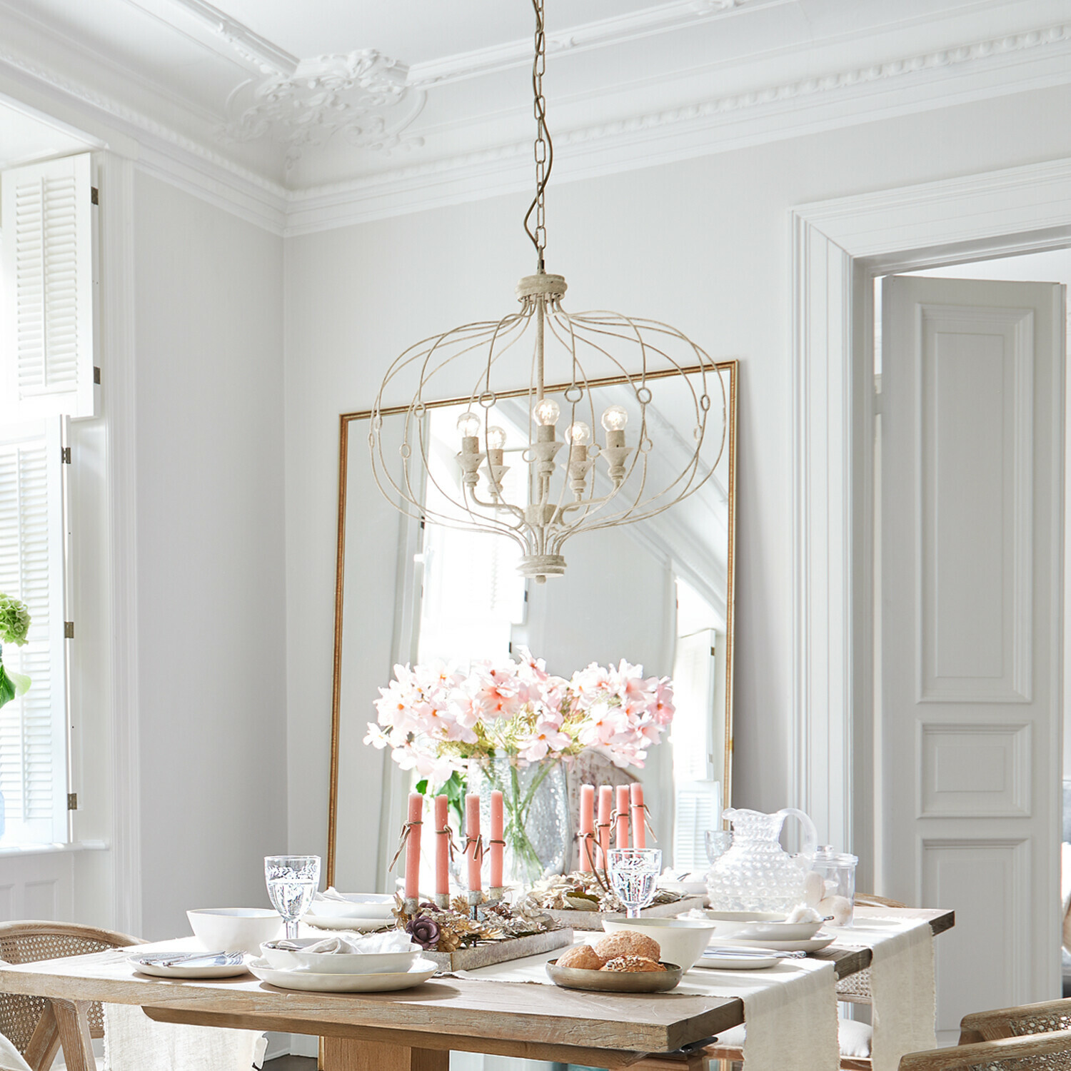 Lampadario Aragonese Sala da pranzo luminosa con tavolo in legno, candele rosa e lampadario metallico vintage sospeso