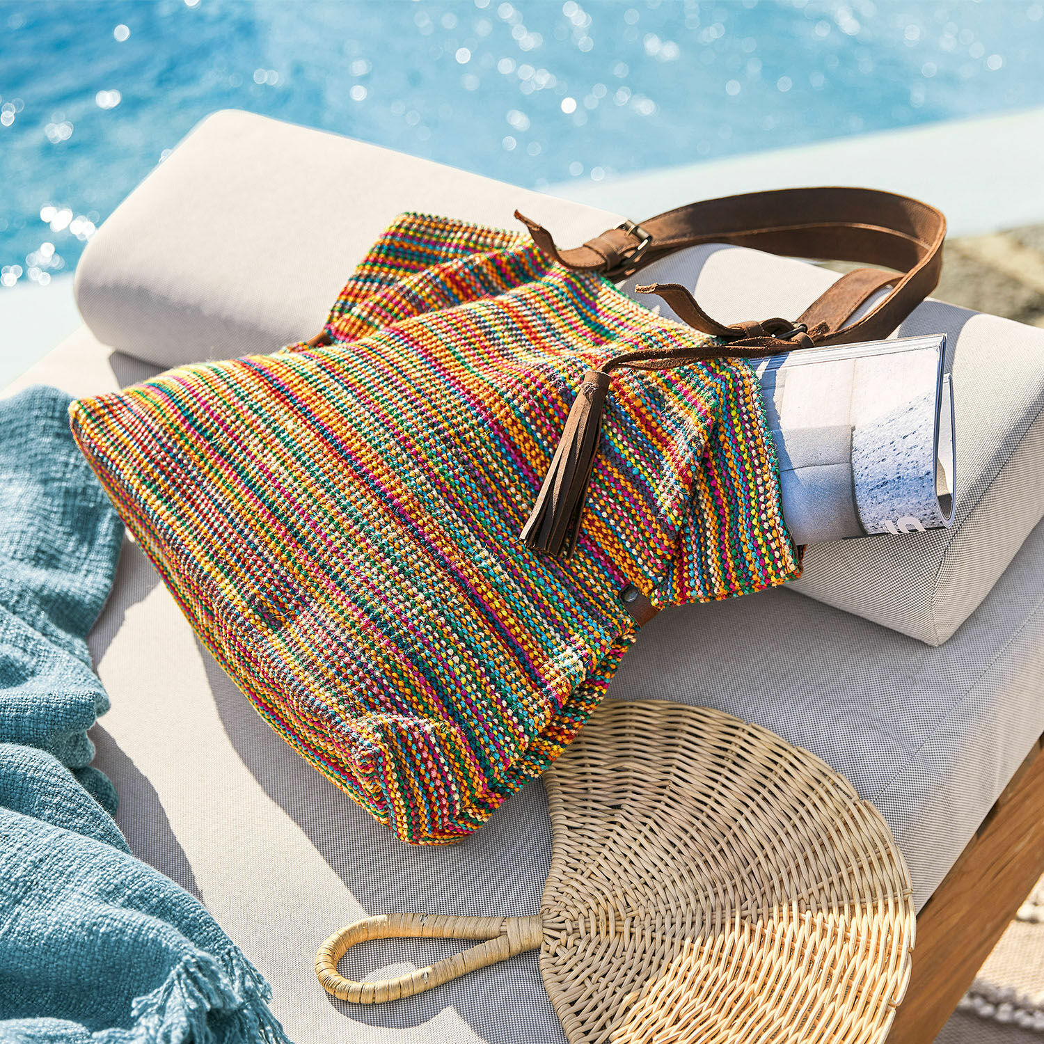 Borsa Gillian Borsa intrecciata multicolore con tracolla marrone su lettino chiaro vicino alla piscina, accessorio estivo