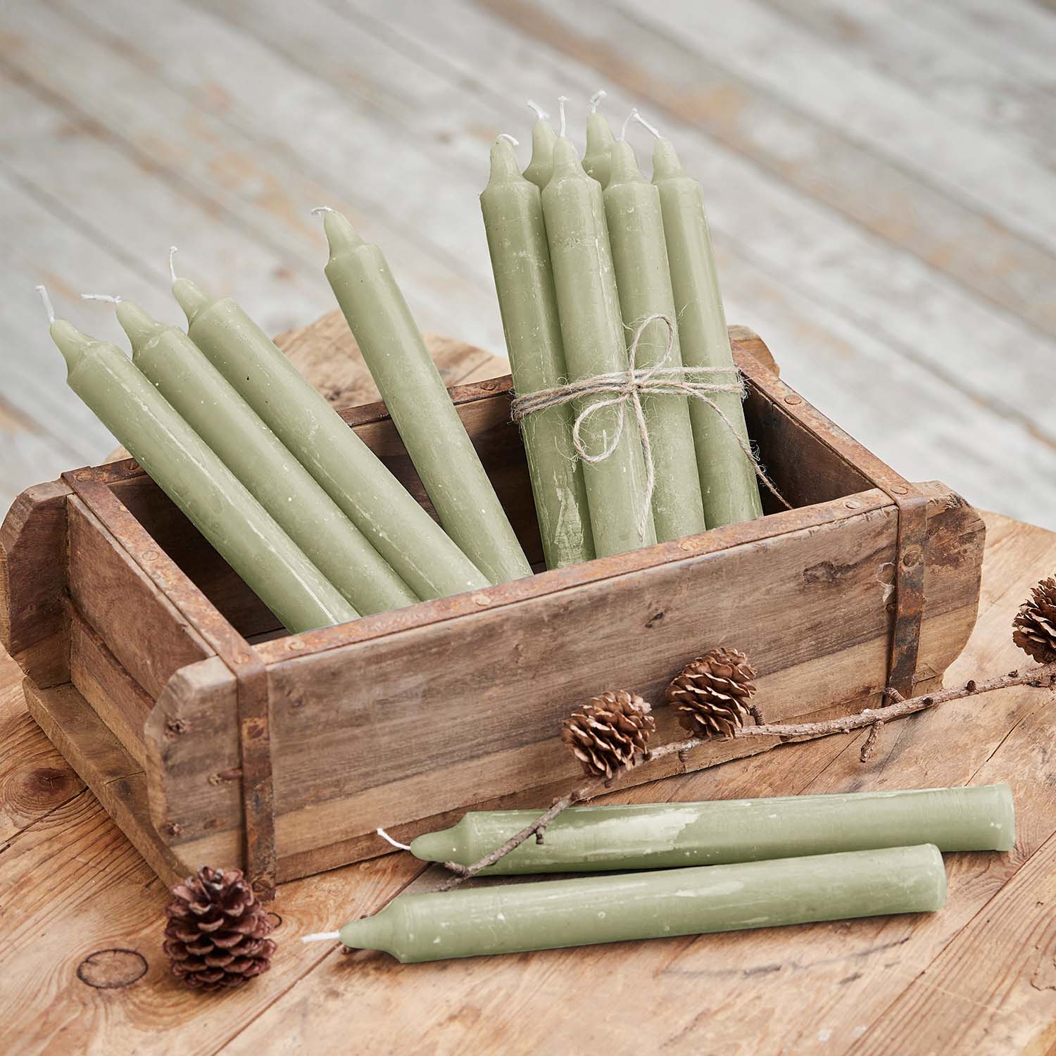 Set di candele verdi in cera in scatola di legno su tavolo rustico con pigne decorative
