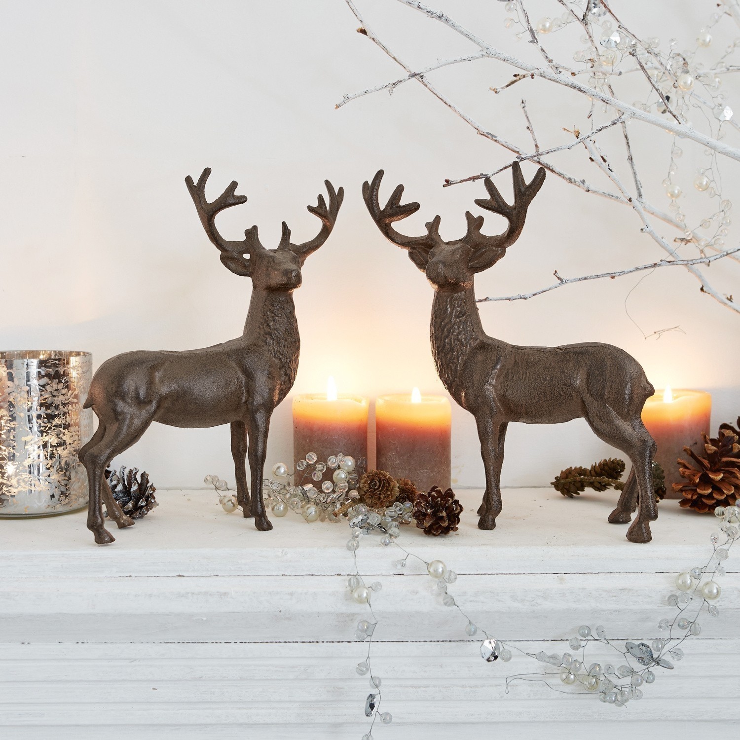 Coppia di cervi decorativi Friends Due decorazioni di cervi in metallo marrone su mensola bianca con candele e pigne