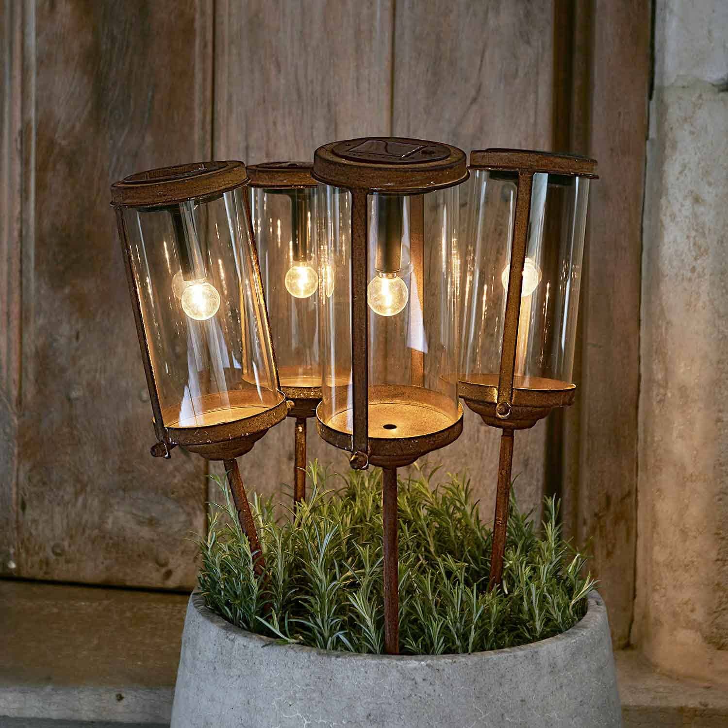 Set di quattro lampade da giardino arrugginite con paralumi in vetro e supporti metallici in vaso