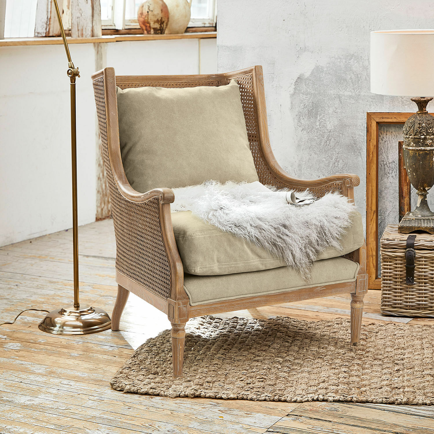 Poltrona Greenbrier Poltrona in legno e rattan con cuscino beige e coperta bianca in pelliccia su tappeto naturale