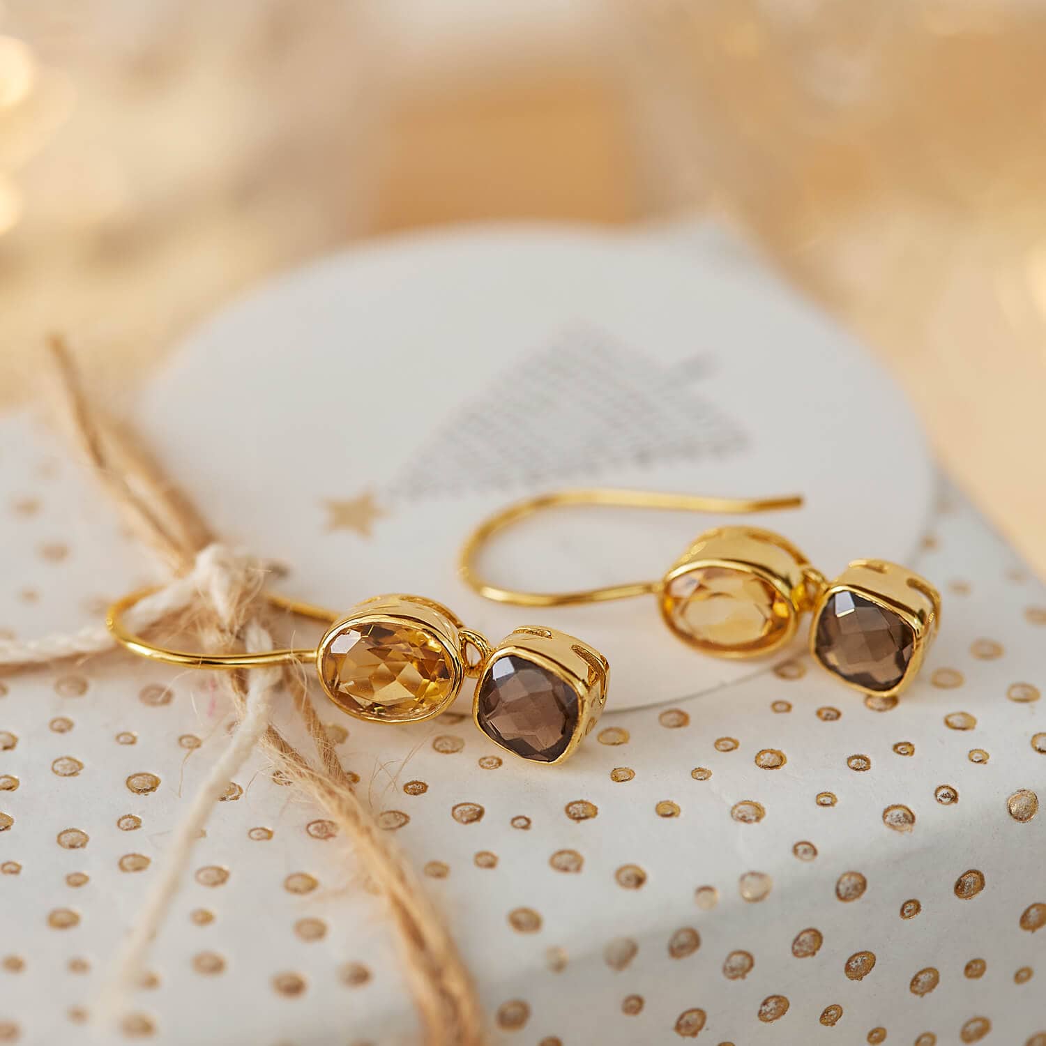 Orecchini dorati con pietre sfaccettate marroni e ambra su sfondo decorativo festivo