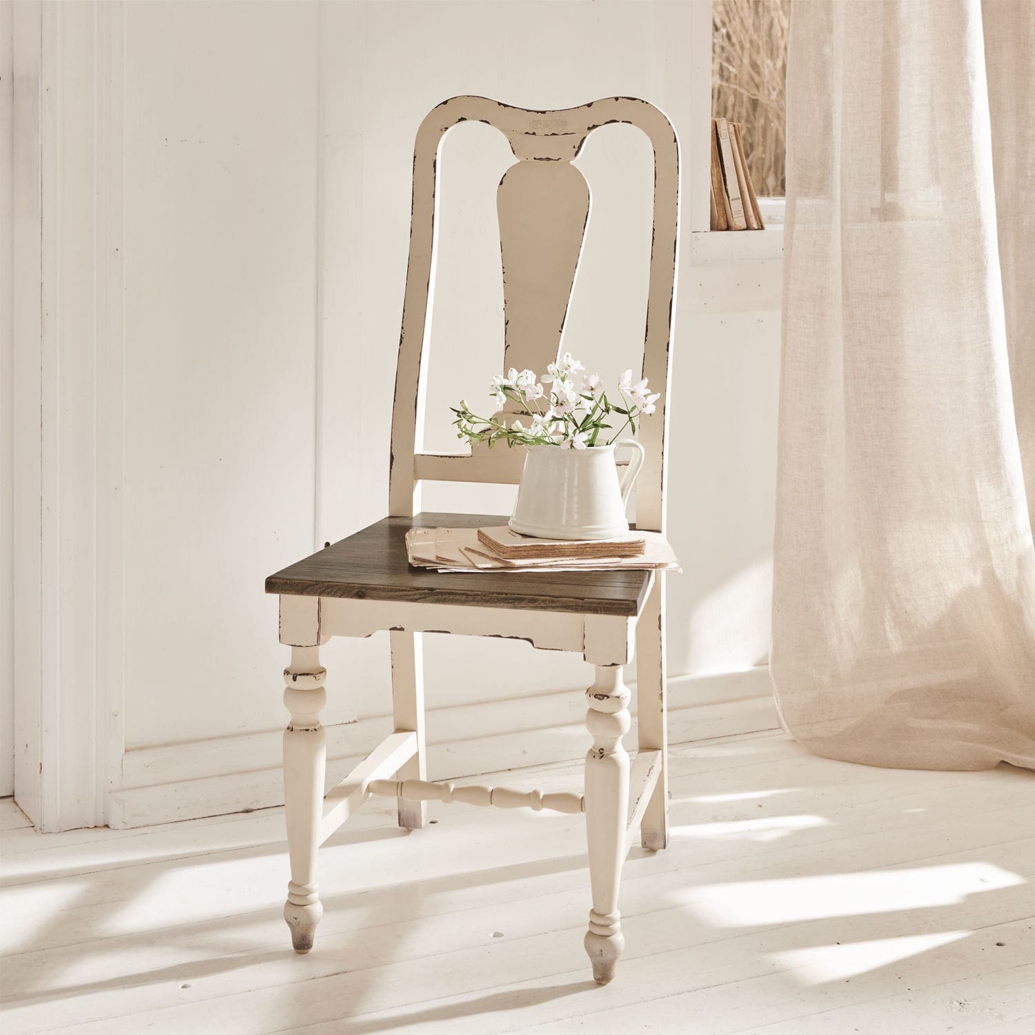Sedia Harry Sedia vintage in legno bianco con seduta scura e brocca con fiori in ambiente luminoso
