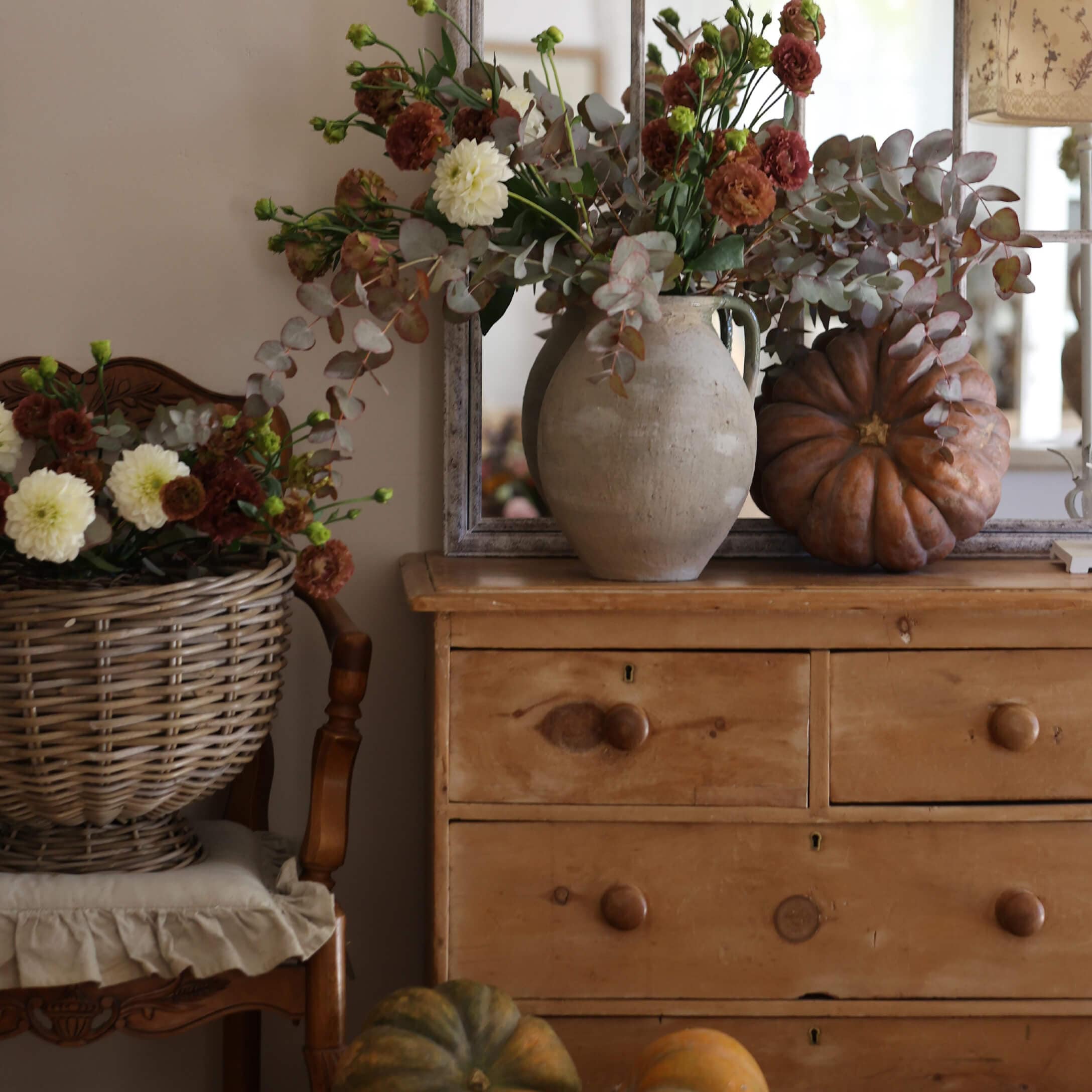 Cassettiera rustica in legno con vaso in terracotta, bouquet autunnale e zucche decorative in ambiente accogliente