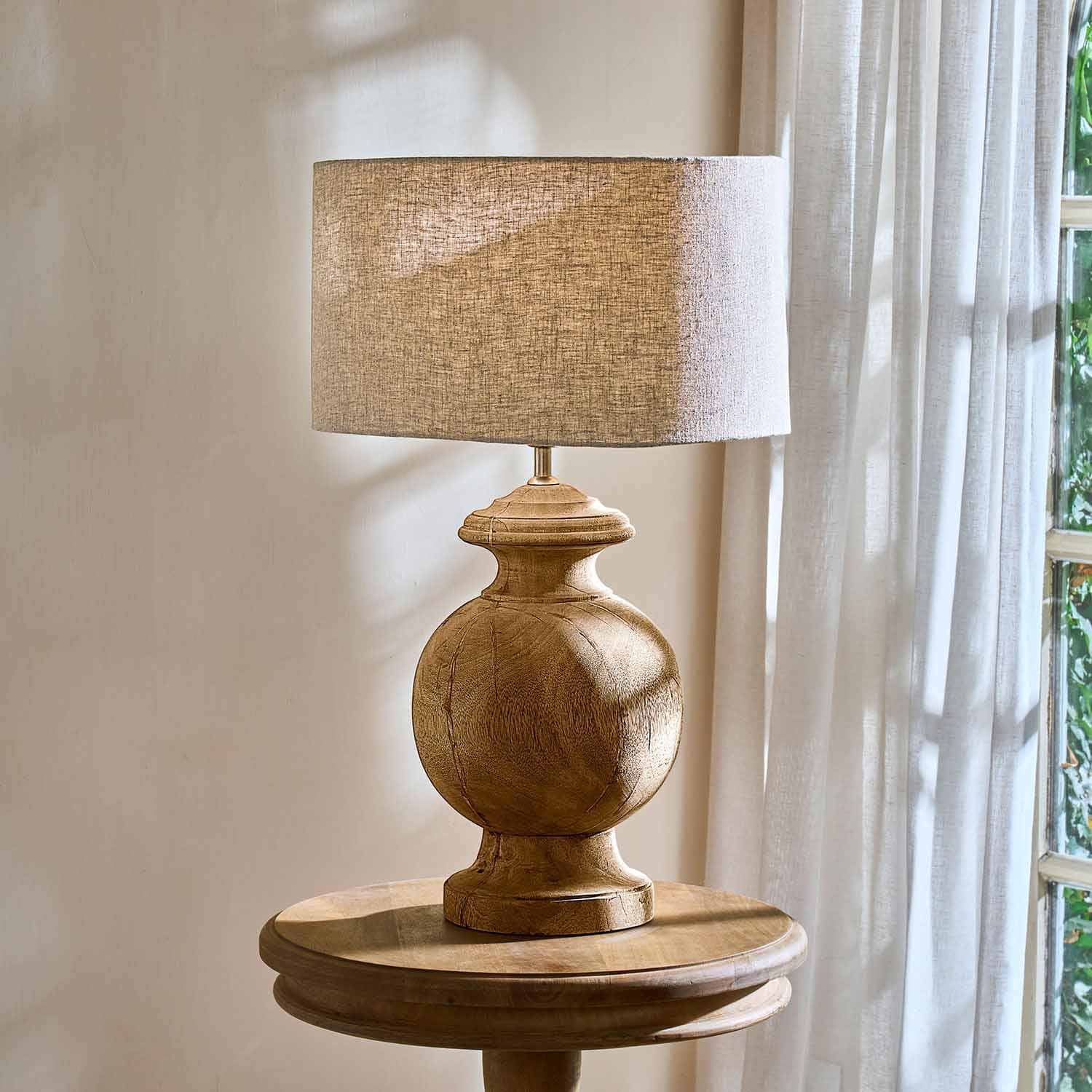 Lampada da tavolo con base in legno e paralume beige su tavolo rotondo vicino alla finestra