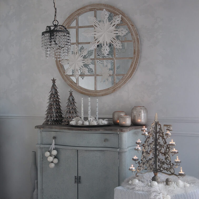 Credenza grigia con decorazioni natalizie, alberi di metallo e candelabro vintage con candele accese
