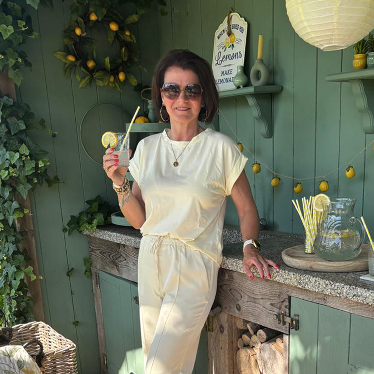 Donna con completo crema si rilassa con limonata davanti a parete verde con decorazioni di limoni