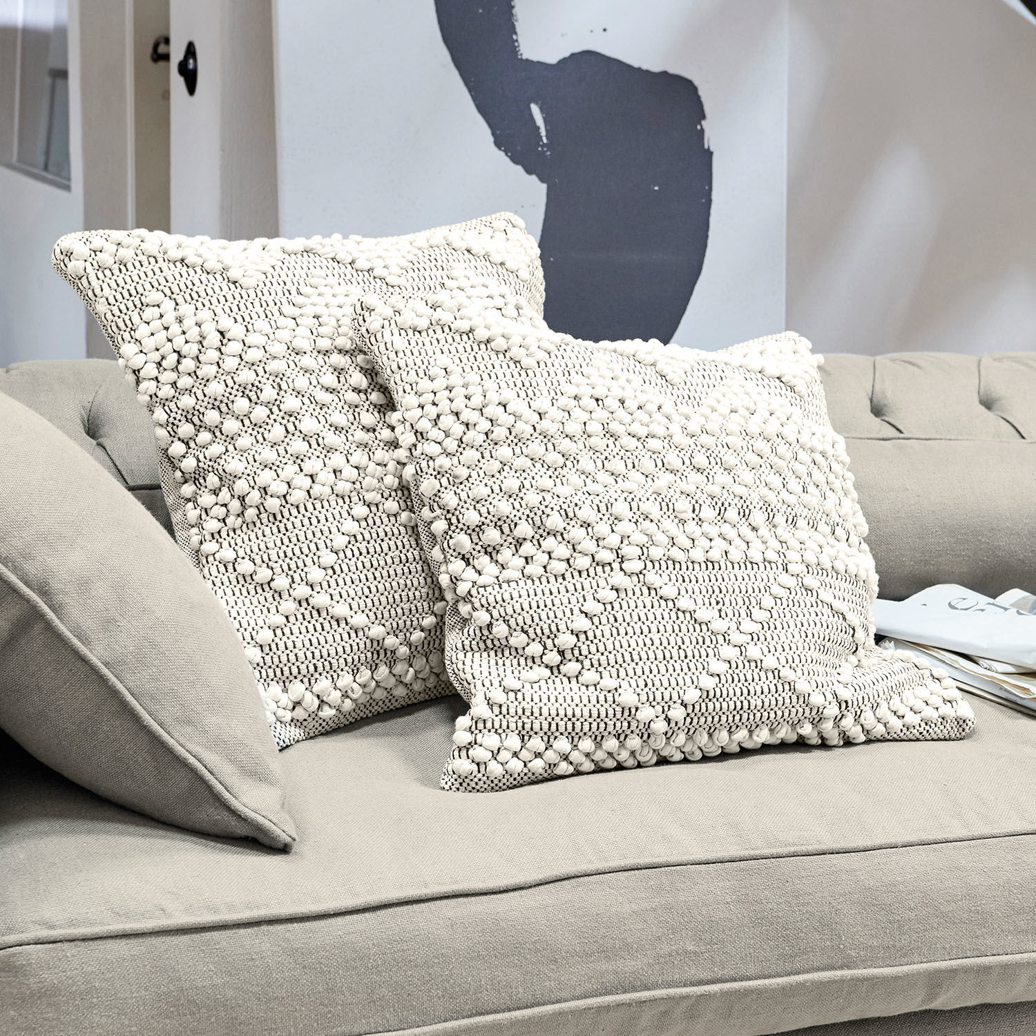 Coppia di copricuscini Hadir Due cuscini decorativi crema in cotone con trama e motivo geometrico su divano grigio